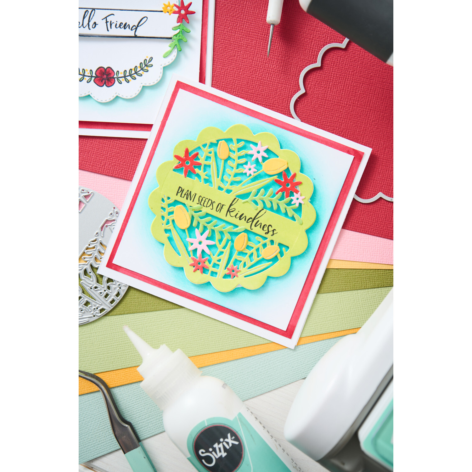 Thinlits Scalloped Circle, Borders & Banners Set zeigt bunte Papierkunst mit floralen Mustern. Sizzix-Werkzeuge und Kleber im Hintergrund.