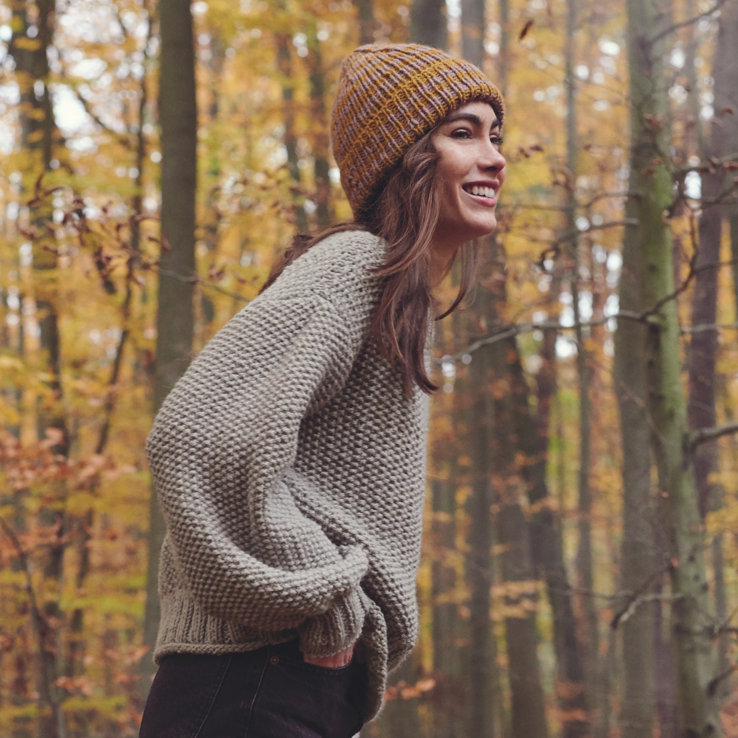 Strickanleitung Pullover und Streifenmütze aus Essentials Alpaca Twist chunky, getragen von einer lächelnden Person im Wald.