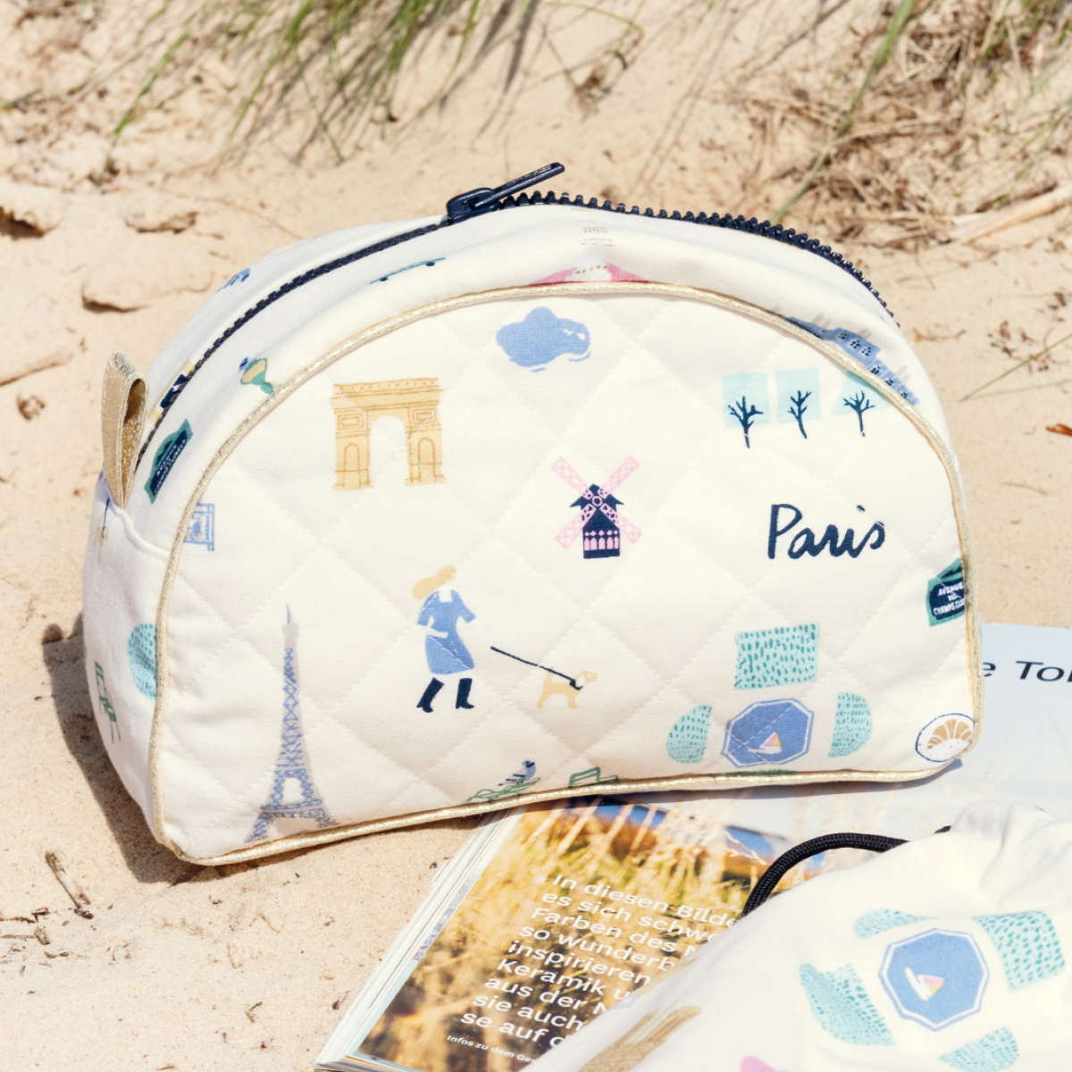 Nähanleitung Beauty Bag mit Paris-Motiven, darunter Eiffelturm und Windmühle, auf sandigem Hintergrund.