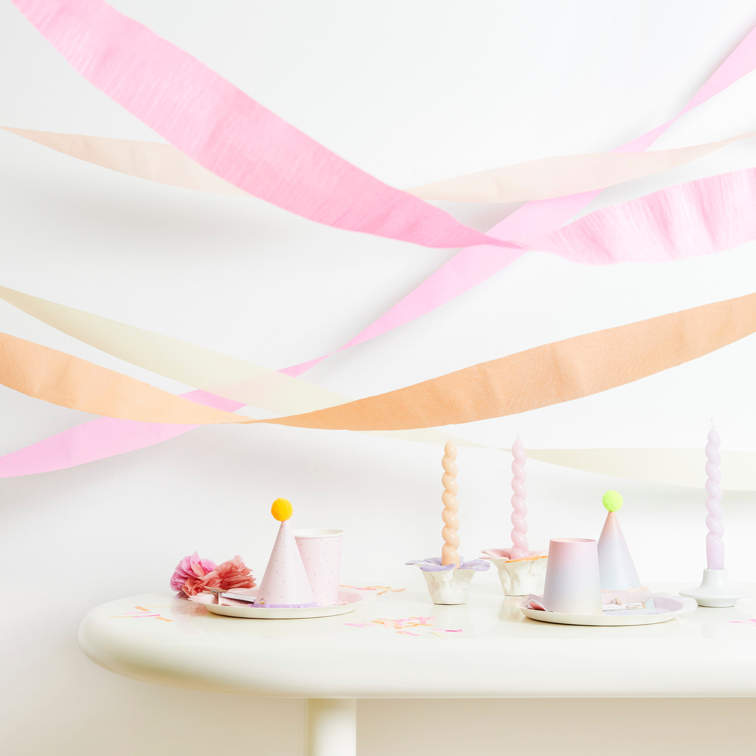 Kreppbänder extra breit Blüten Mix dekorieren einen Tisch mit pastellfarbenen Kerzen und Partyhüten.