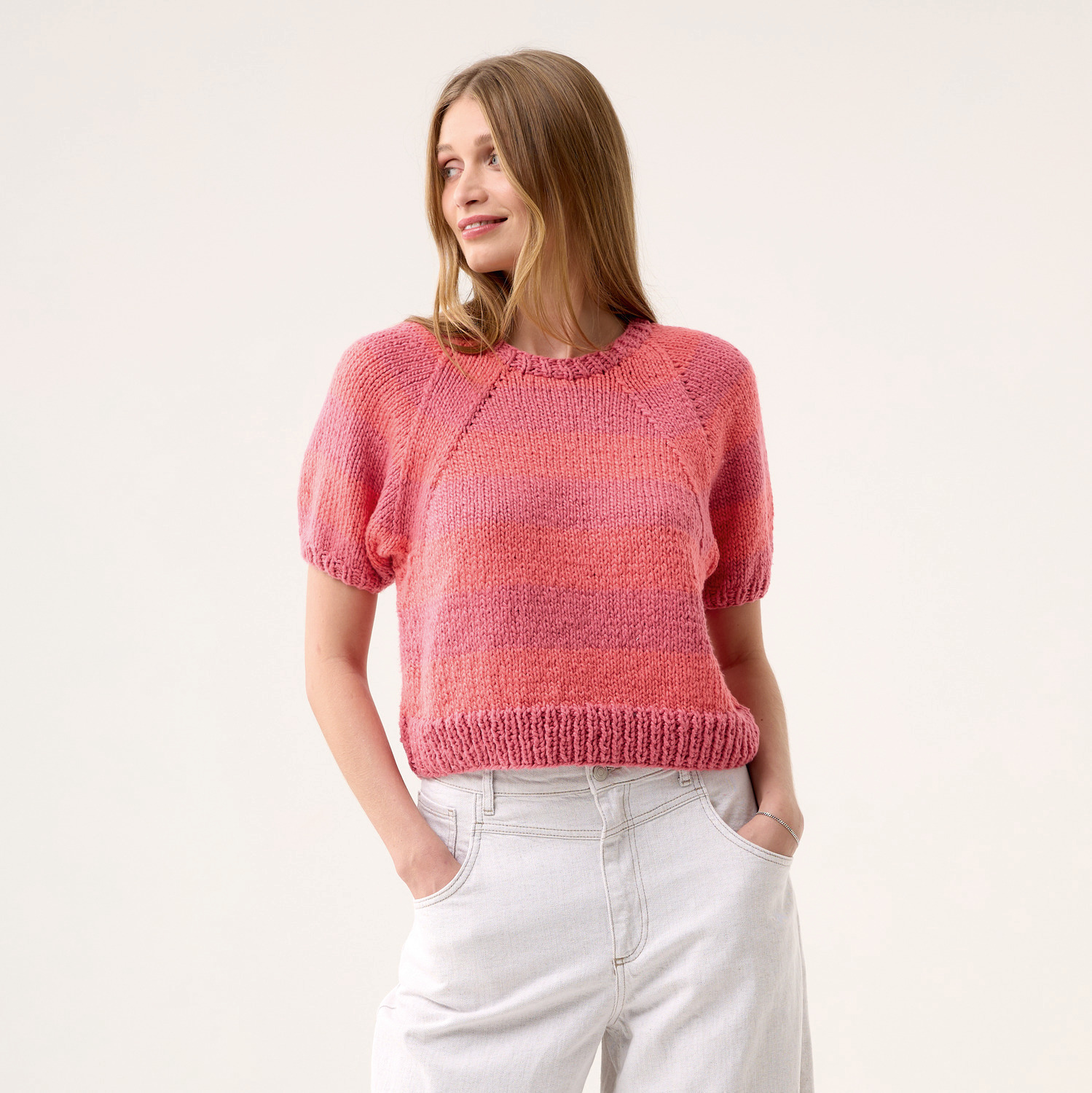 Strickset Shirt Modell 01: Frau trägt ein kurzärmeliges, rosa gestricktes Shirt mit Rundhalsausschnitt.