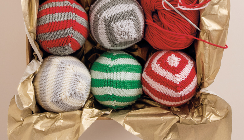 Strickanleitung Weihnachtskugeln: Sechs gestrickte Kugeln in Rot, Grün und Grau in einer goldenen Box.