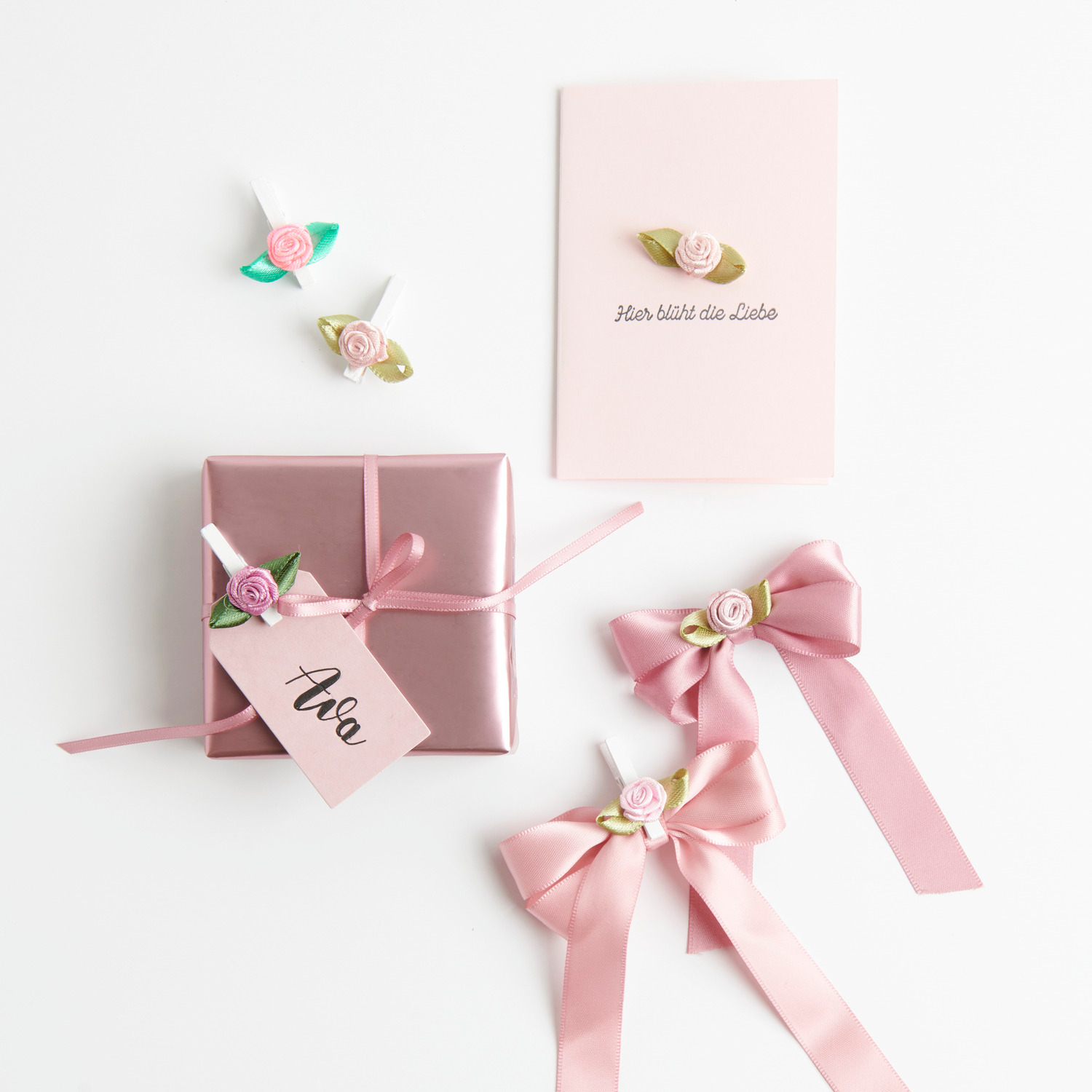 Geschenkpapier Metallic mit Röschenmotiv und Schleife, kombiniert mit Satin-Geschenkband in Beere und Rosa von Rico Design.
