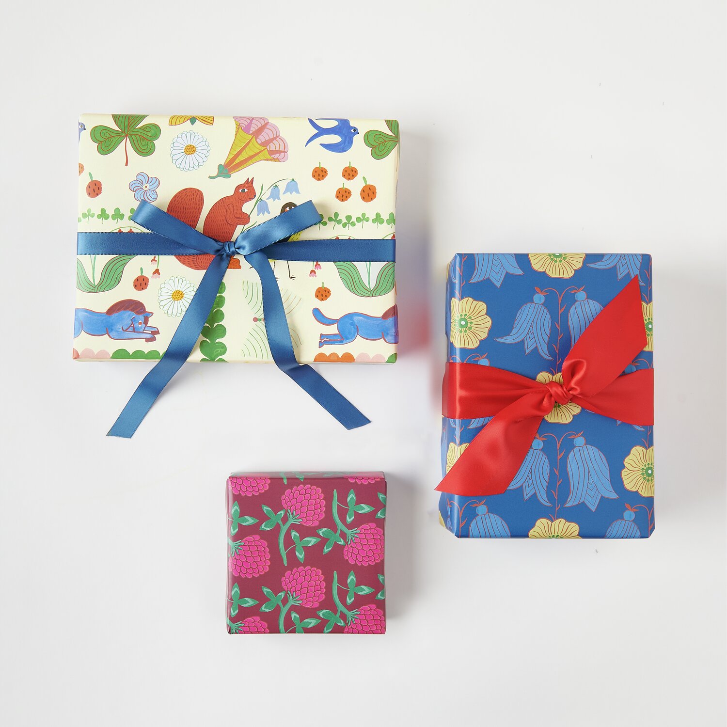 Geschenkpapier Mix Midsommar Magic: Drei Geschenke in buntem Papier mit blauen und roten Schleifen.