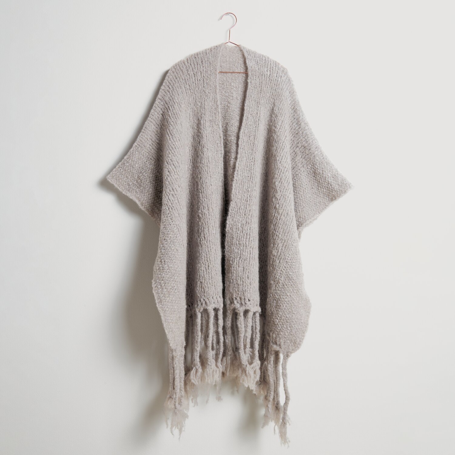 Strickset Poncho Modell 07a aus Die Neue Masche No. 10, beige, mit Fransen, an einem Haken hängend.