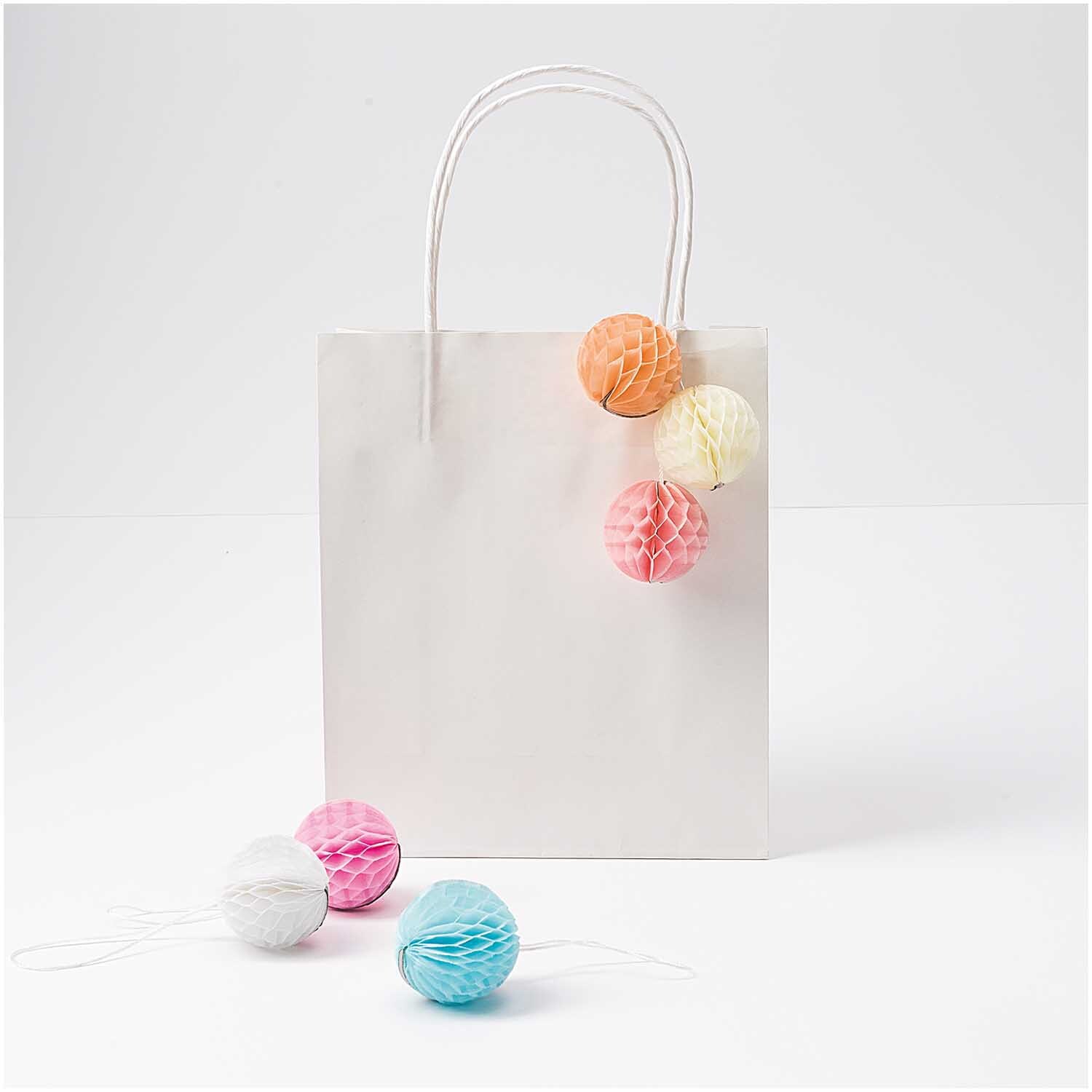 Mini-Wabenbälle 4cm 6 Stück von Rico Design in Pastellfarben an einer weißen Geschenktüte.