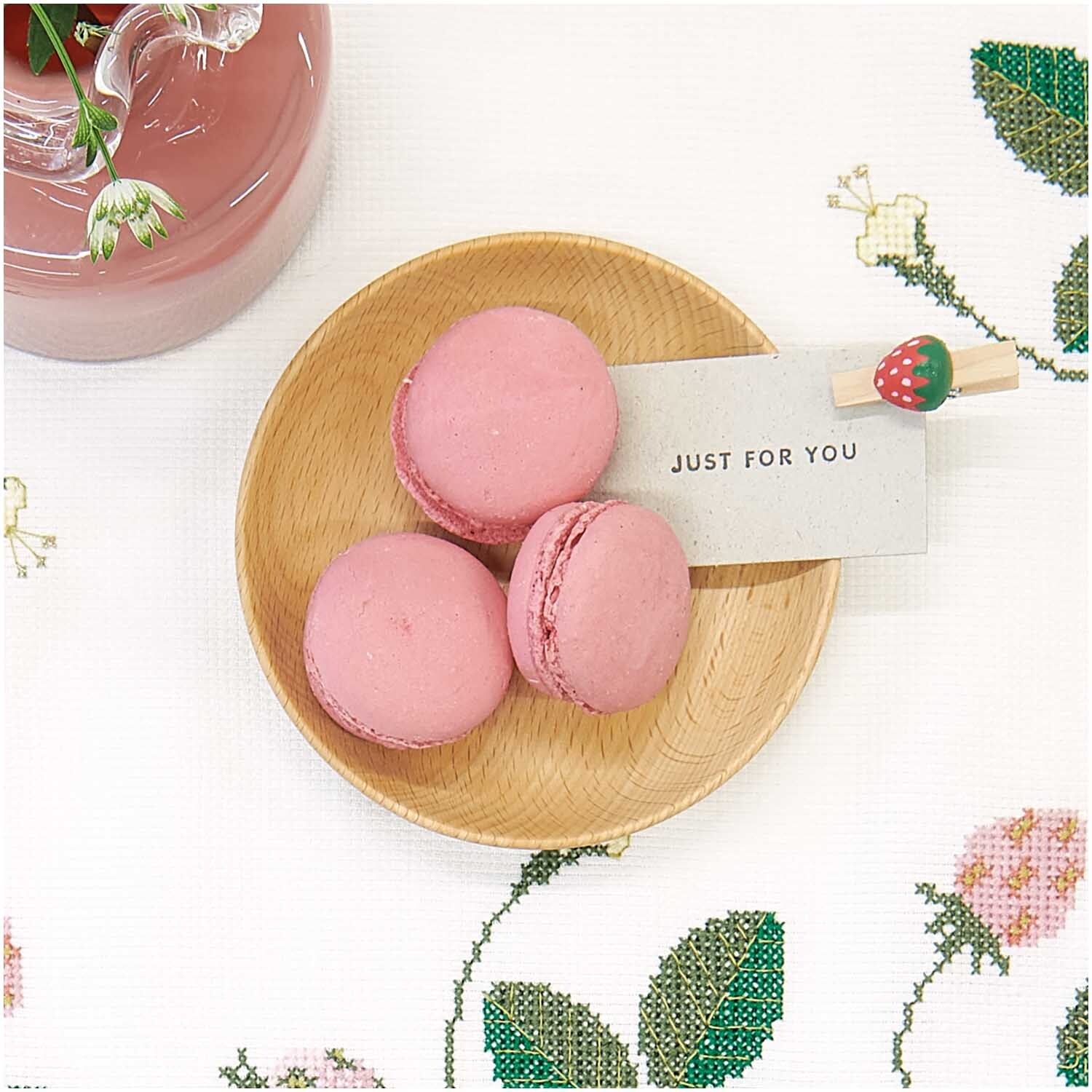 Holzklammern Erdbeere 8 Stück von Rico Design: Rosa Macarons auf Holzplatte mit Erdbeerklammer und Grußkarte auf bestickter Tischdecke.