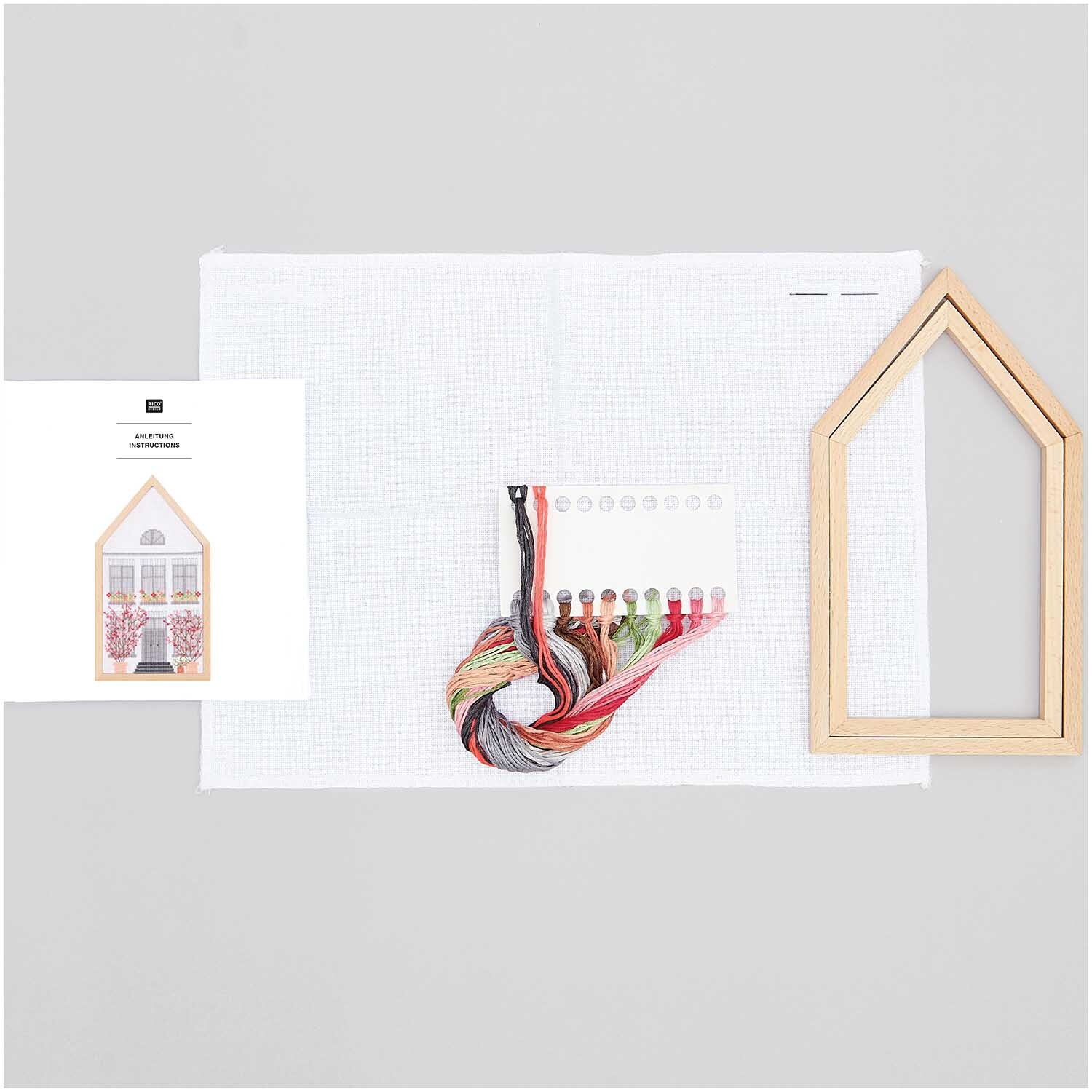 Stickpackung Frühlingshaus mittel von Rico Design mit Holzrahmen, Garn und Anleitung auf weißem Hintergrund.
