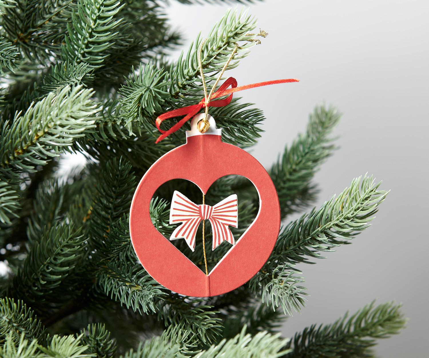 Paper Poetry Papierornament: Rotes Herzdesign mit Schleife, hängend an einem Tannenzweig.