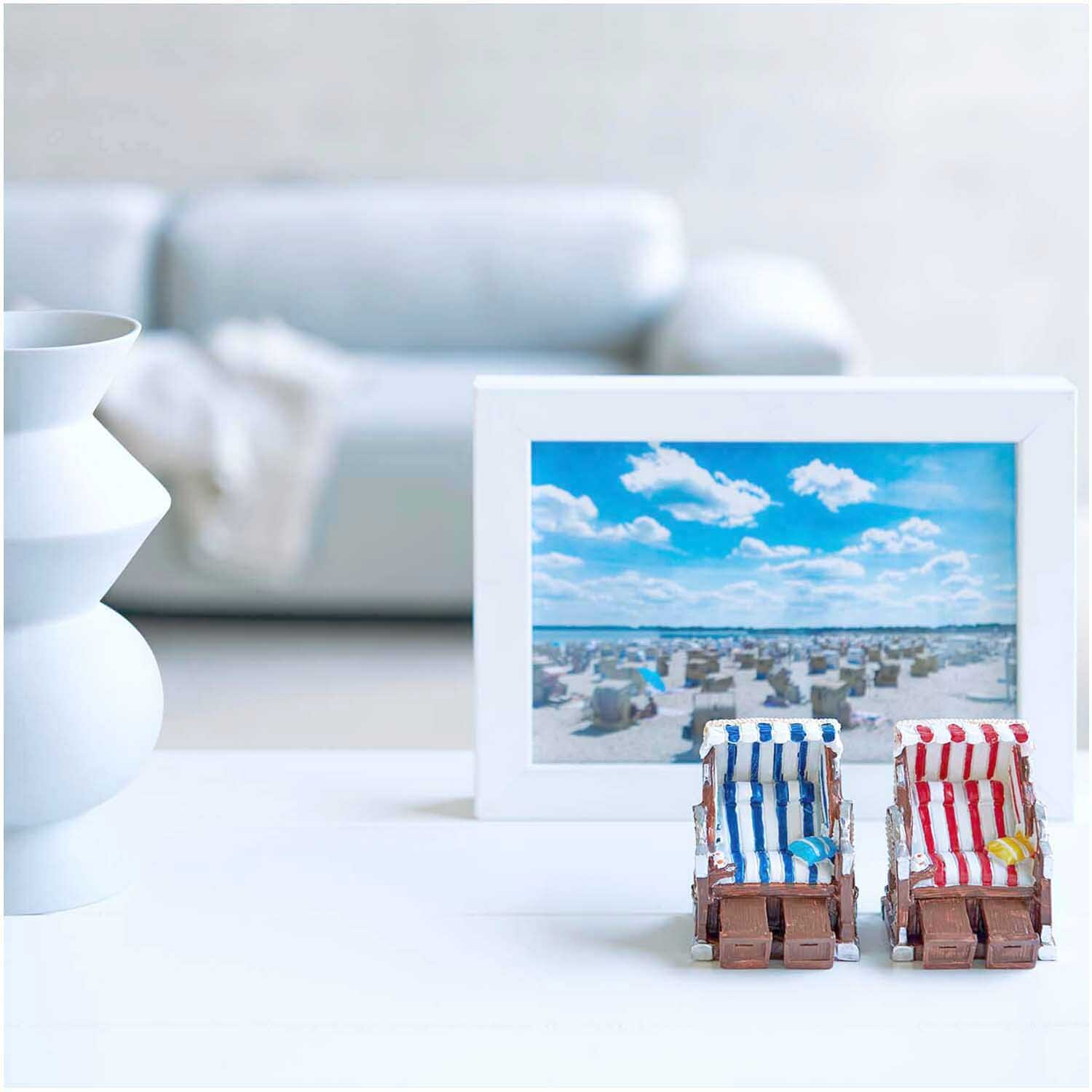 Deko-Strandkorb blau-weiß 5x6,5cm vor einem Strandbild, neben einer weißen Vase auf einem Tisch.