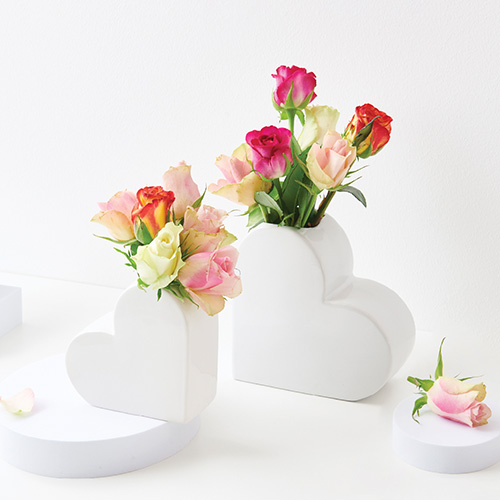 Weiße Vasen in Herzform und verschiedenen Größen, mit Rosen befüllt. Fotosetting weiße Ecke.