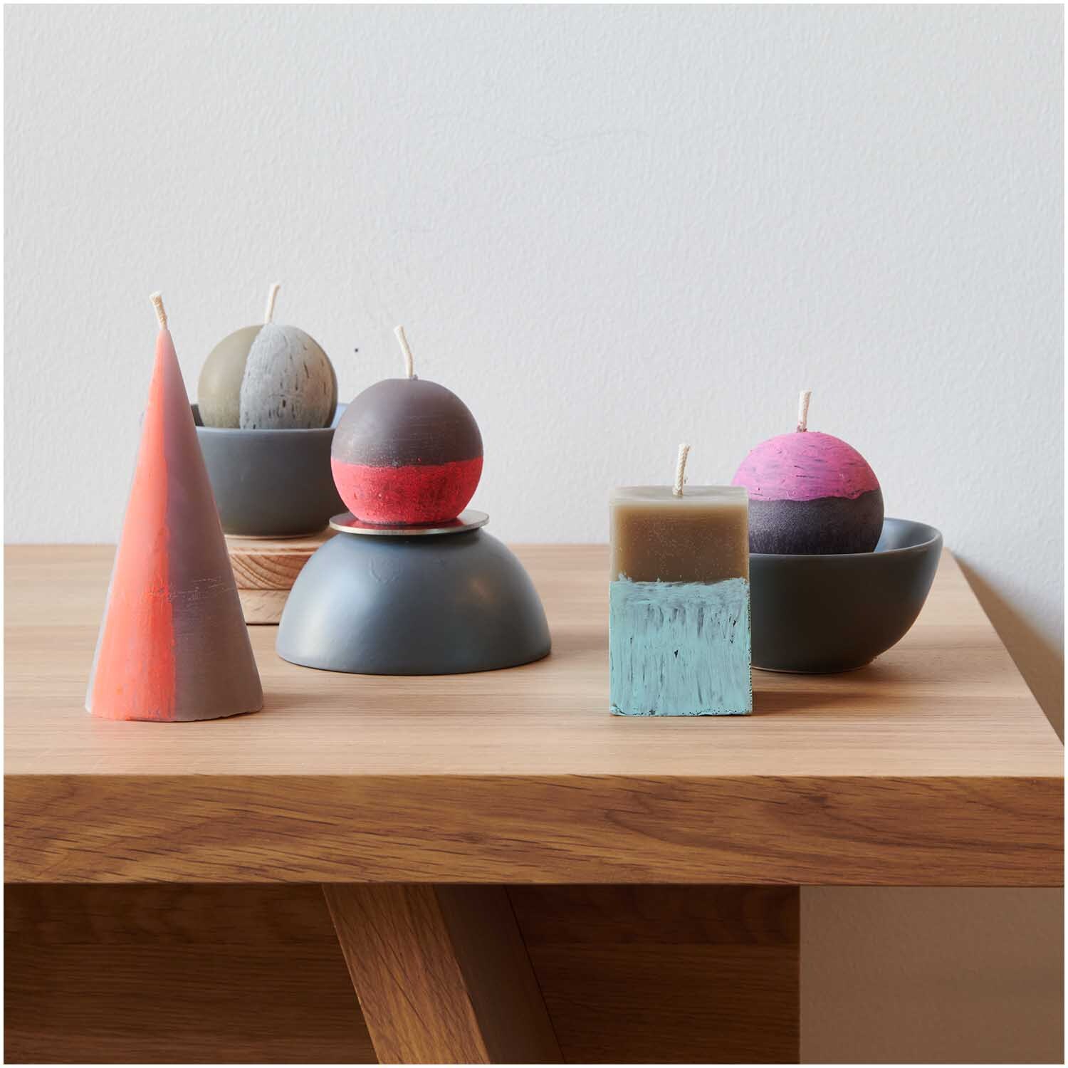 Kerzengießform Kugel 74x74x65mm: Verschiedene bunte Kerzenformen auf einem Holztisch arrangiert.