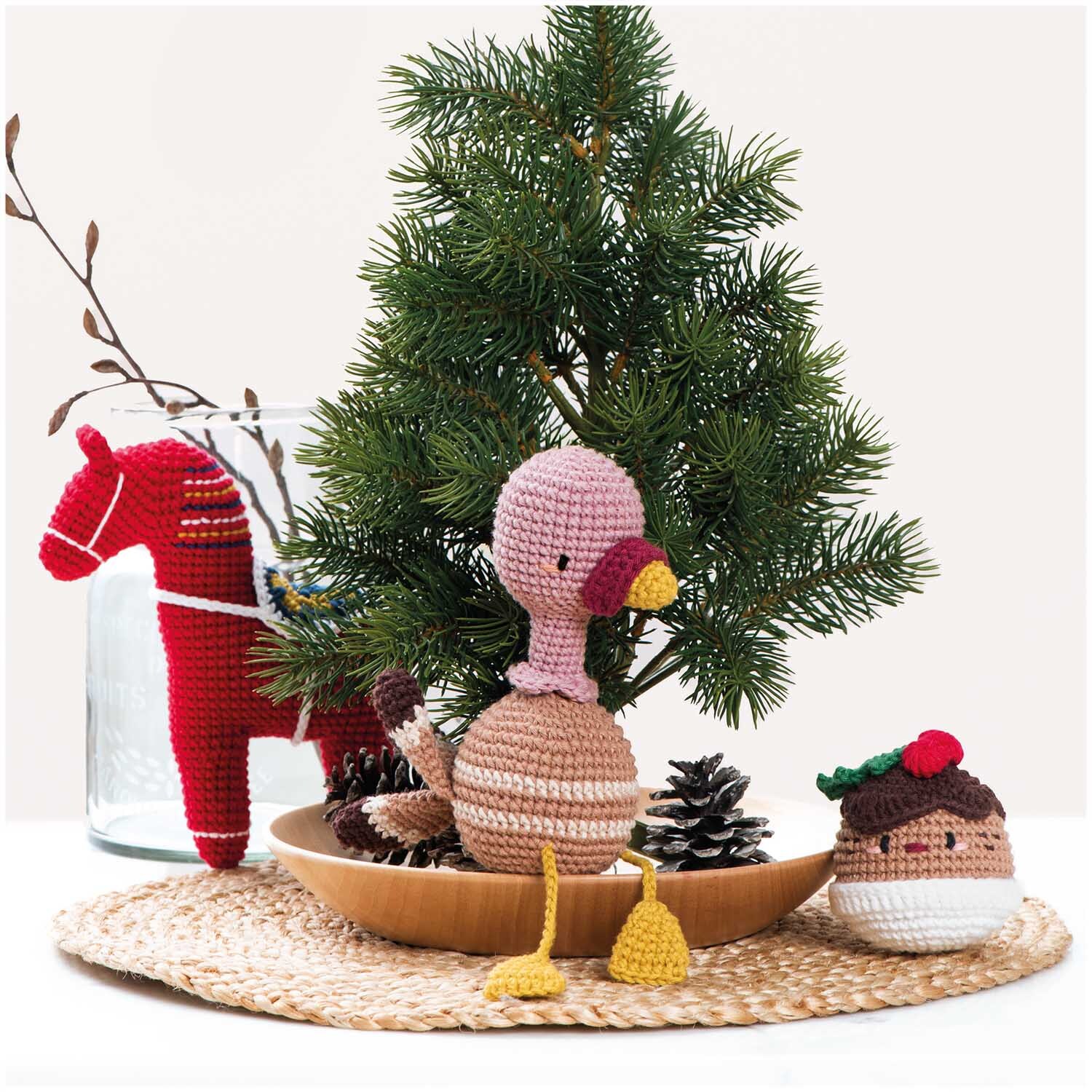 Creative Ricorumi dk: Gehäkelte Figuren vor einem kleinen Tannenbaum, dekoriert mit einem roten Pferd und einem Tannenzapfen.