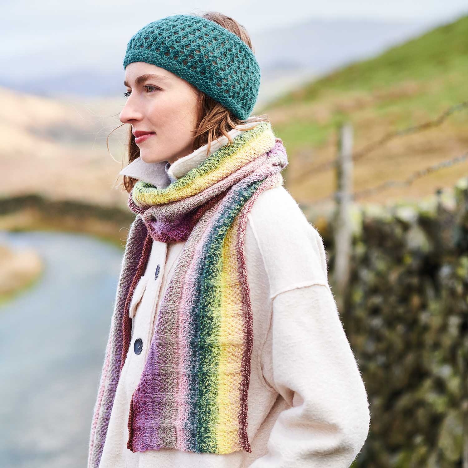 Strickanleitung Schal aus Creative Alpaca Dégradé Lucky 8: Frau trägt bunten Schal und grünes Stirnband in ländlicher Umgebung.