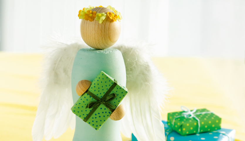 Bastelanleitung Engel aus Beton: Ein Engel mit Flügeln und Blumenkranz hält ein grünes Geschenk.