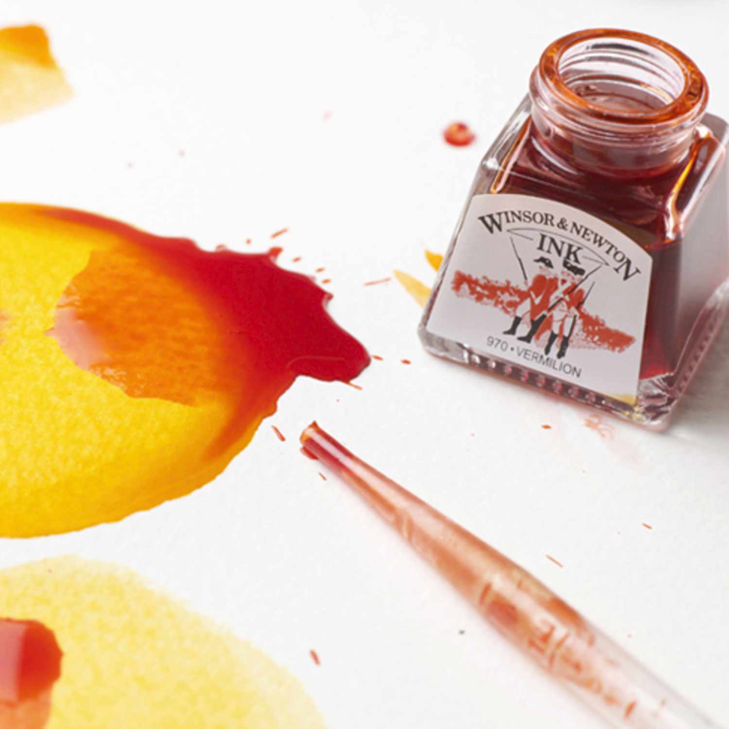 Zeichentusche 14ml von Winsor & Newton neben einem Pinsel und leuchtenden Farbklecksen auf Papier.