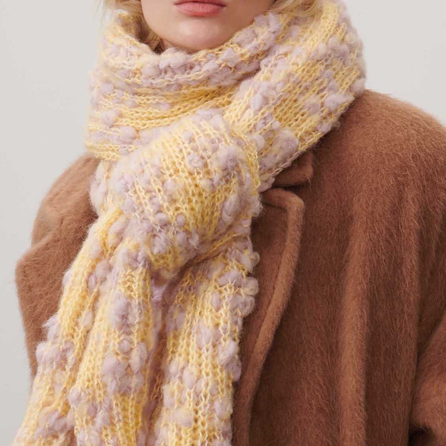 Fashion Alpaca Vibes aran: Weicher, gestrickter Schal in Vanille-Flieder von Rico Design, getragen über einem braunen Mantel.