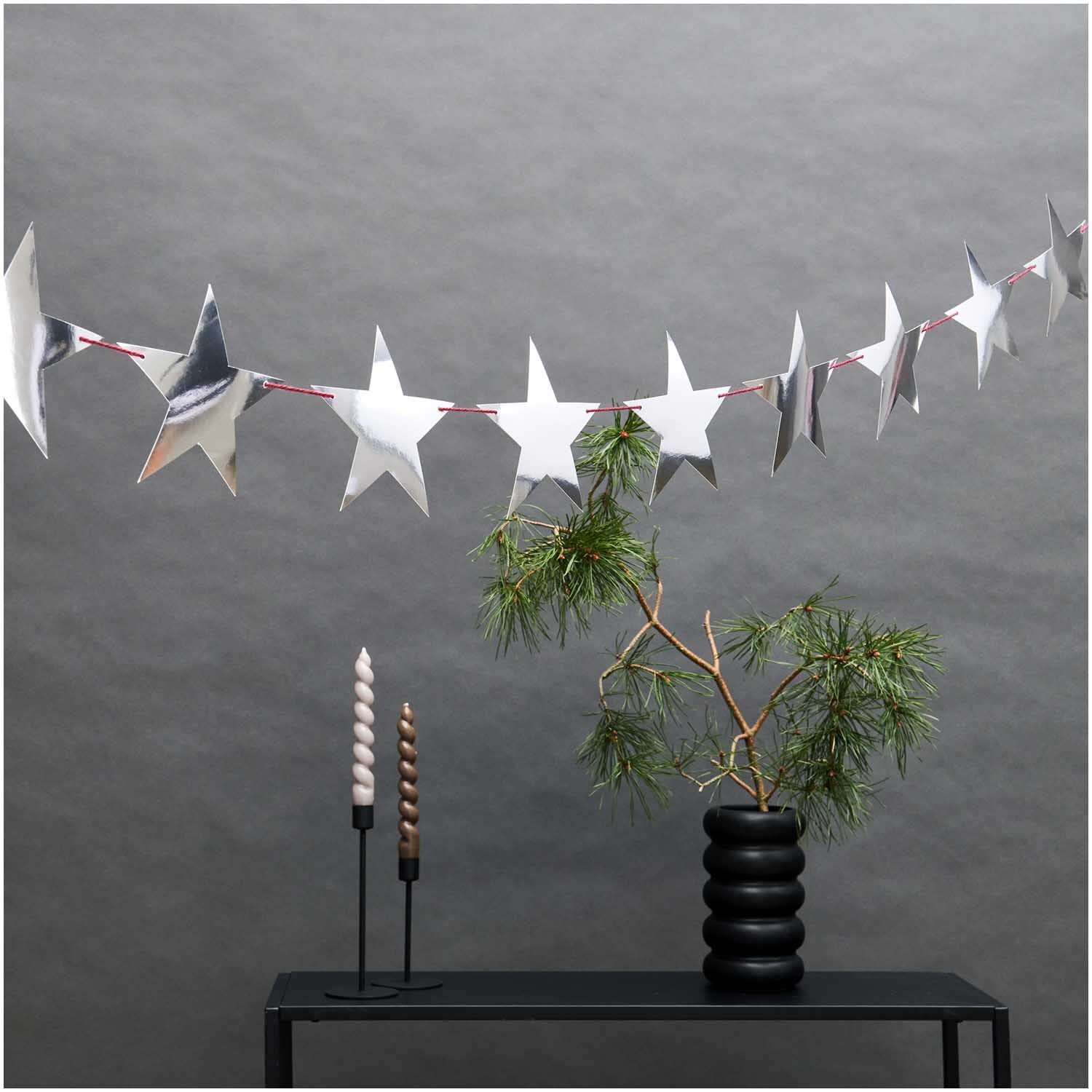 Paper Poetry Girlande Sterne silber 3m, dekorativ über einem Tisch mit Pflanzen und Kerzen.