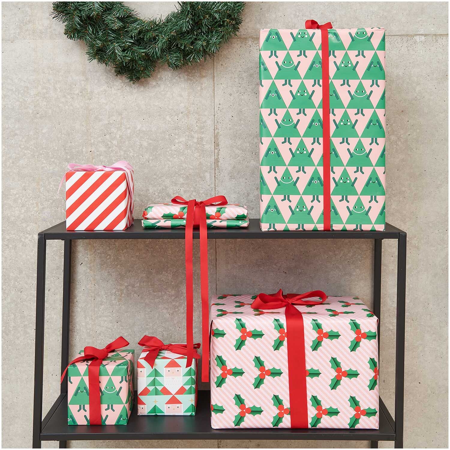 Paper Poetry Geschenkpapier mit Weihnachtsmann- und Tannenbaum-Muster, dekoriert auf einem Regal. Ideal für festliche Anlässe.