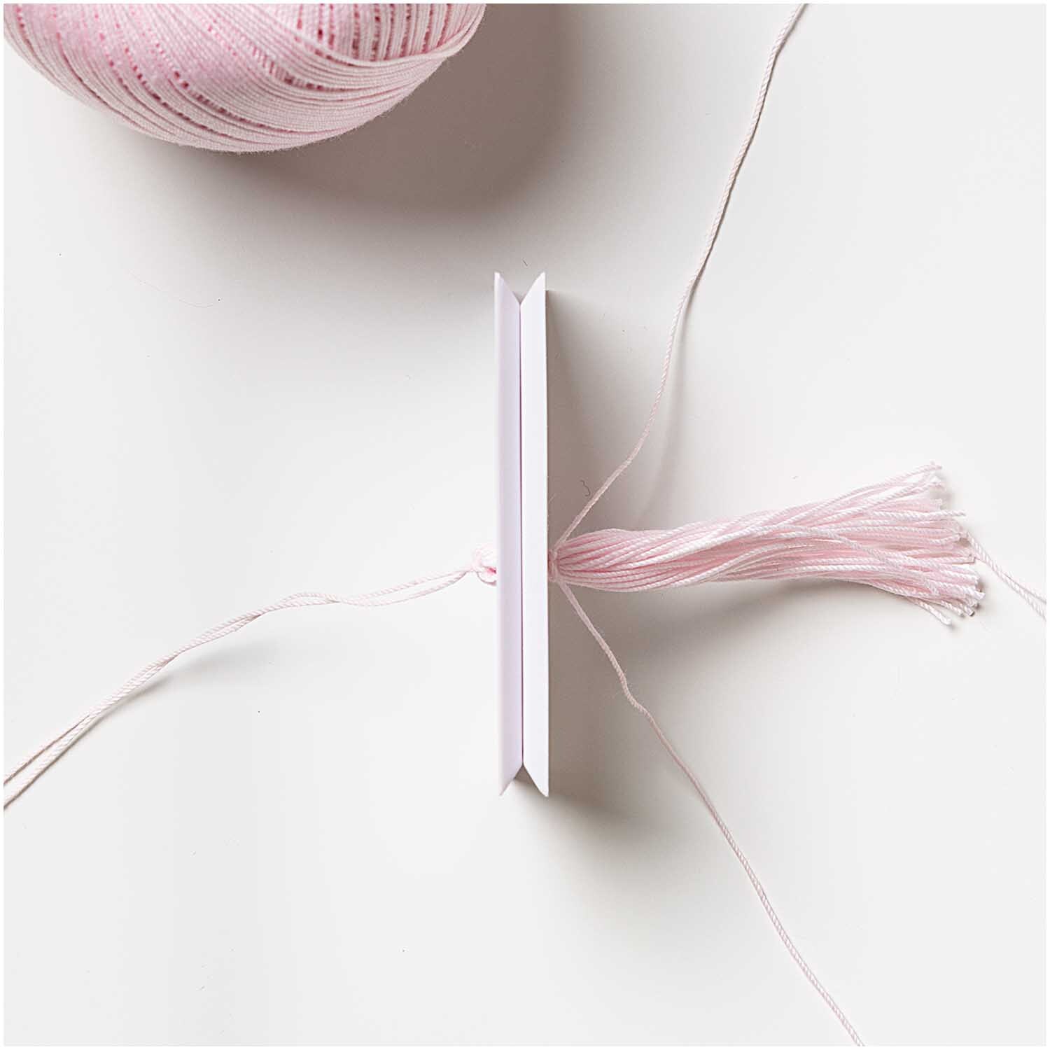Tassel Maker von Rico Design: Ein Werkzeug zur Herstellung von Quasten mit rosa Garn auf weißem Hintergrund.