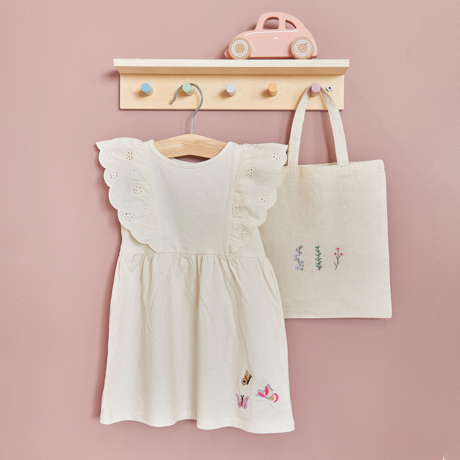 Tragetasche für Kinder natur, 24x28cm, hängt neben einem Kleid an einer Wand mit Haken.
