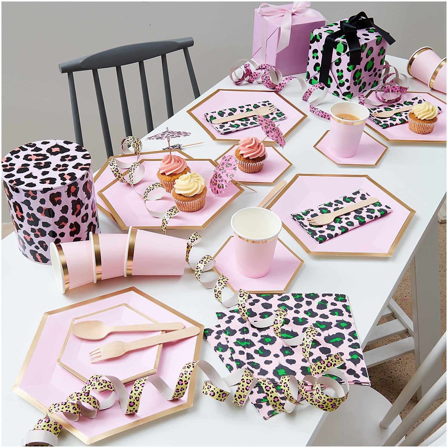 Luftschlangen Acid Leo gold 3,8m auf einem Tisch mit rosa Geschirr und Geschenkboxen in Leopardenmuster.