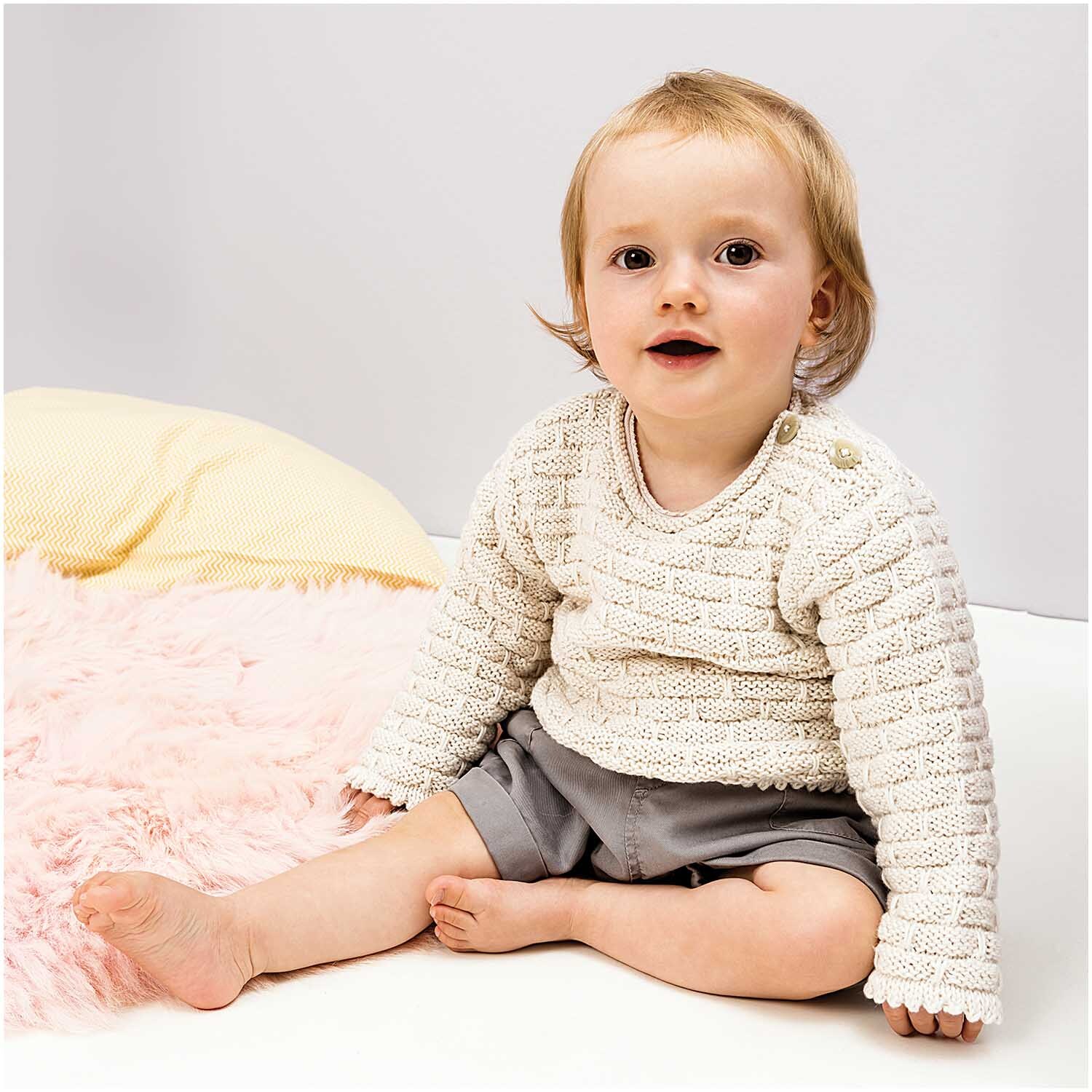 Rico Baby Cotton Soft dk: Ein Baby trägt einen gestrickten Pullover, sitzt auf einer weichen Decke.
