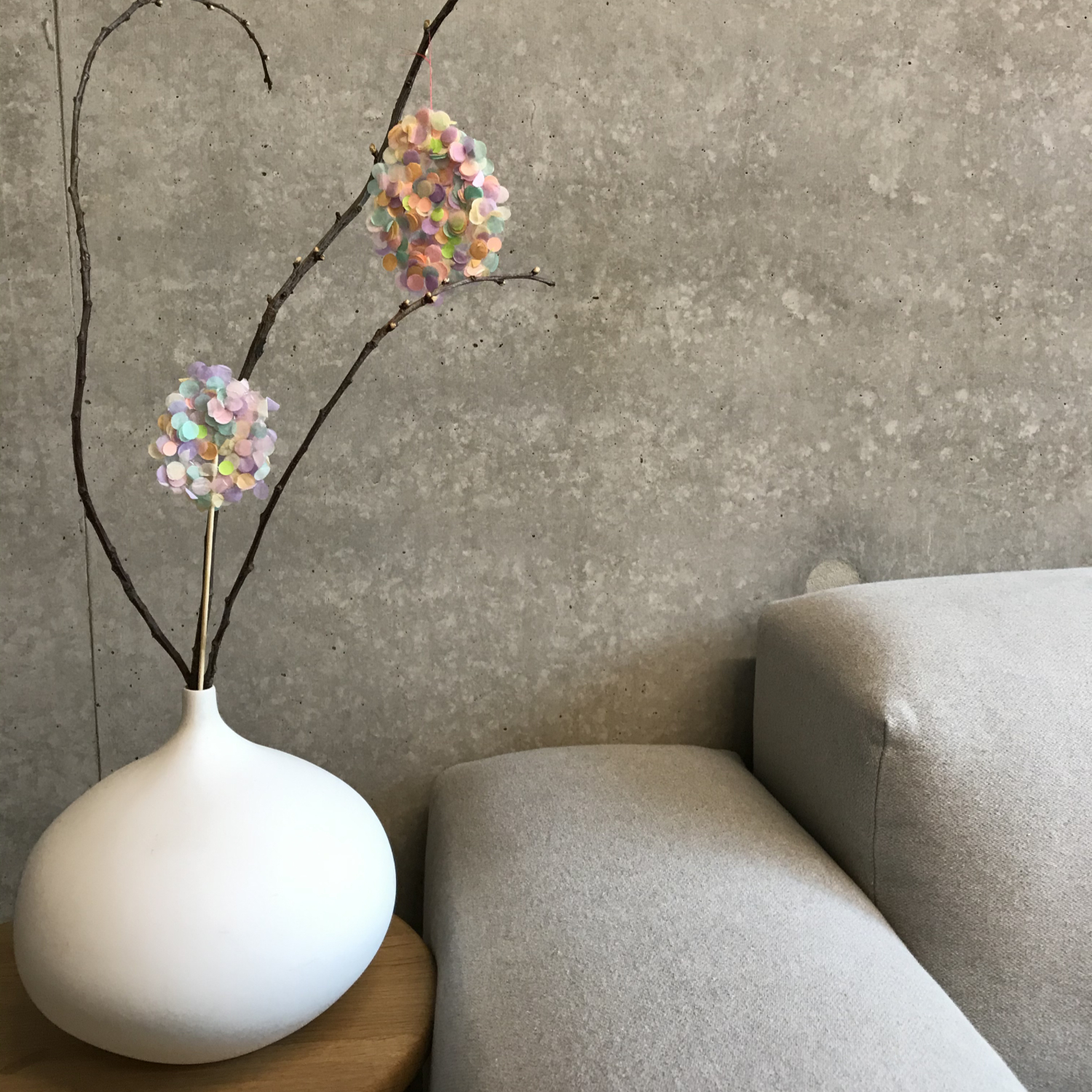 Bastelanleitung Konfetti-Topper und Konfetti-Deko: Bunte Konfetti an Zweigen in weißer Vase auf grauem Sofa.