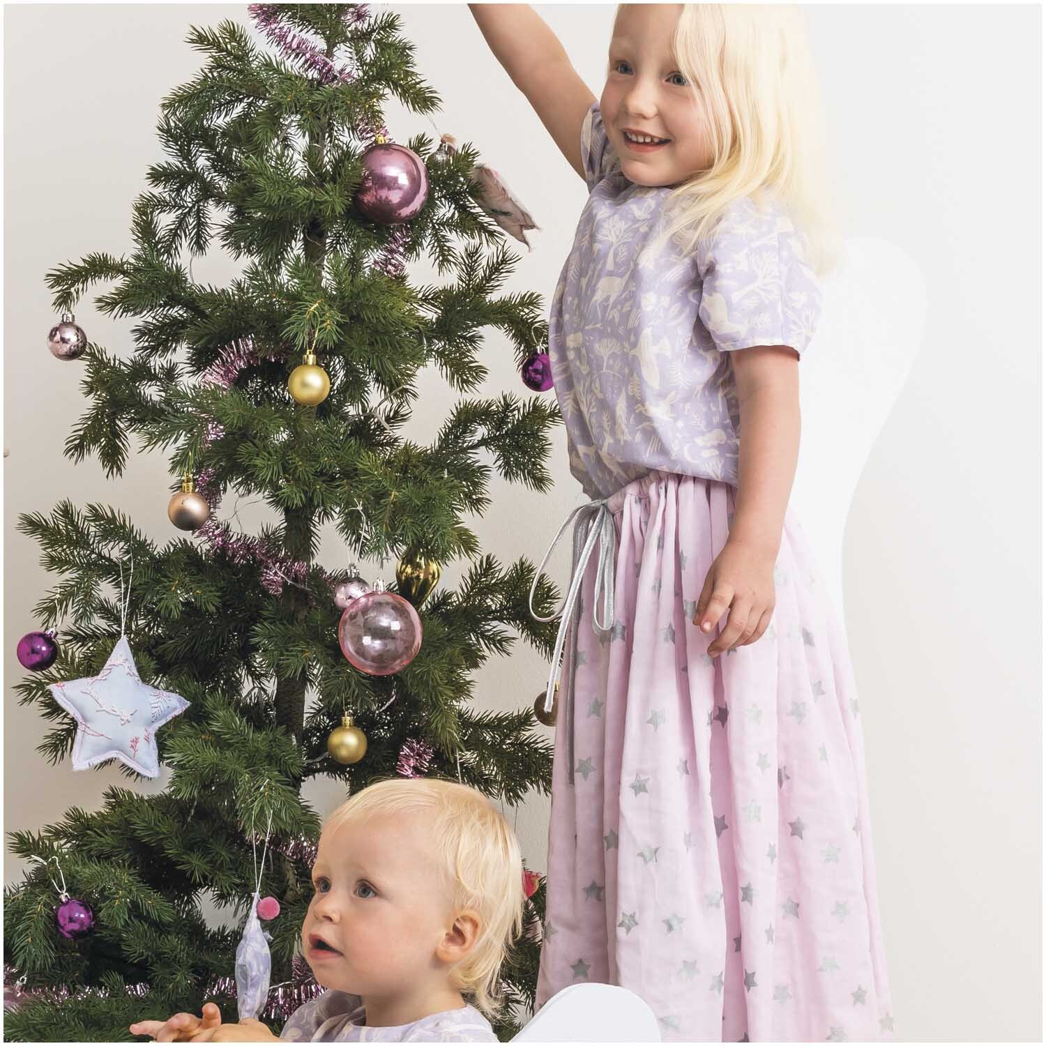 Musselin-Druckstoff Nostalgic Christmas: Zwei Kinder in rosa-metallic Kleidung neben einem geschmückten Weihnachtsbaum.
