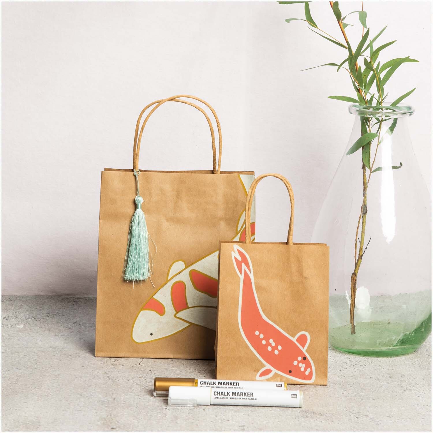 Kreidestifte Flüssigkreide Set Natur 3mm 6 Farben von Rico Design vor zwei Papiertüten mit Koi-Motiven und einer Vase mit Bambus.
