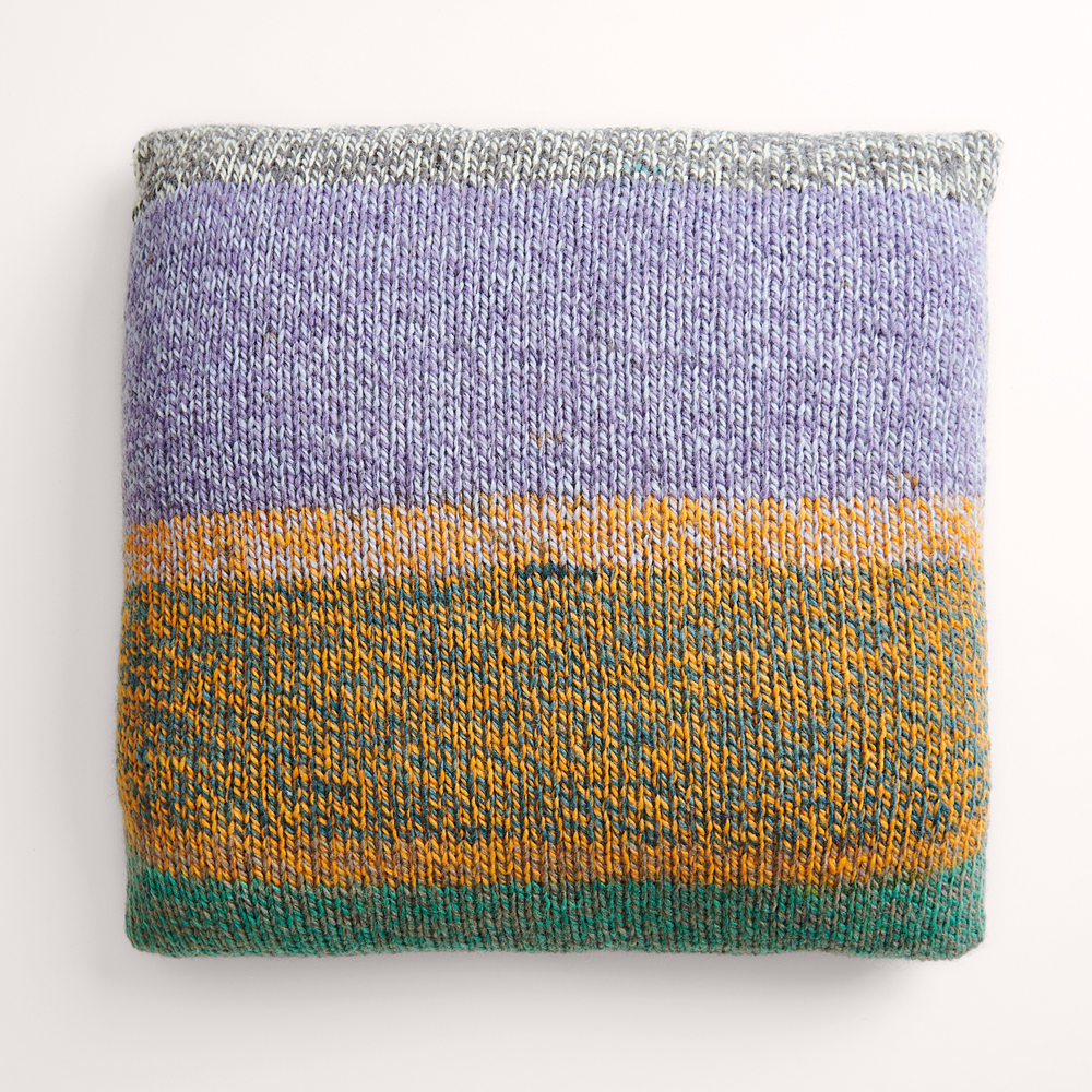 Buntes Kissen auf grauem Hintergrund – zum Strickset
