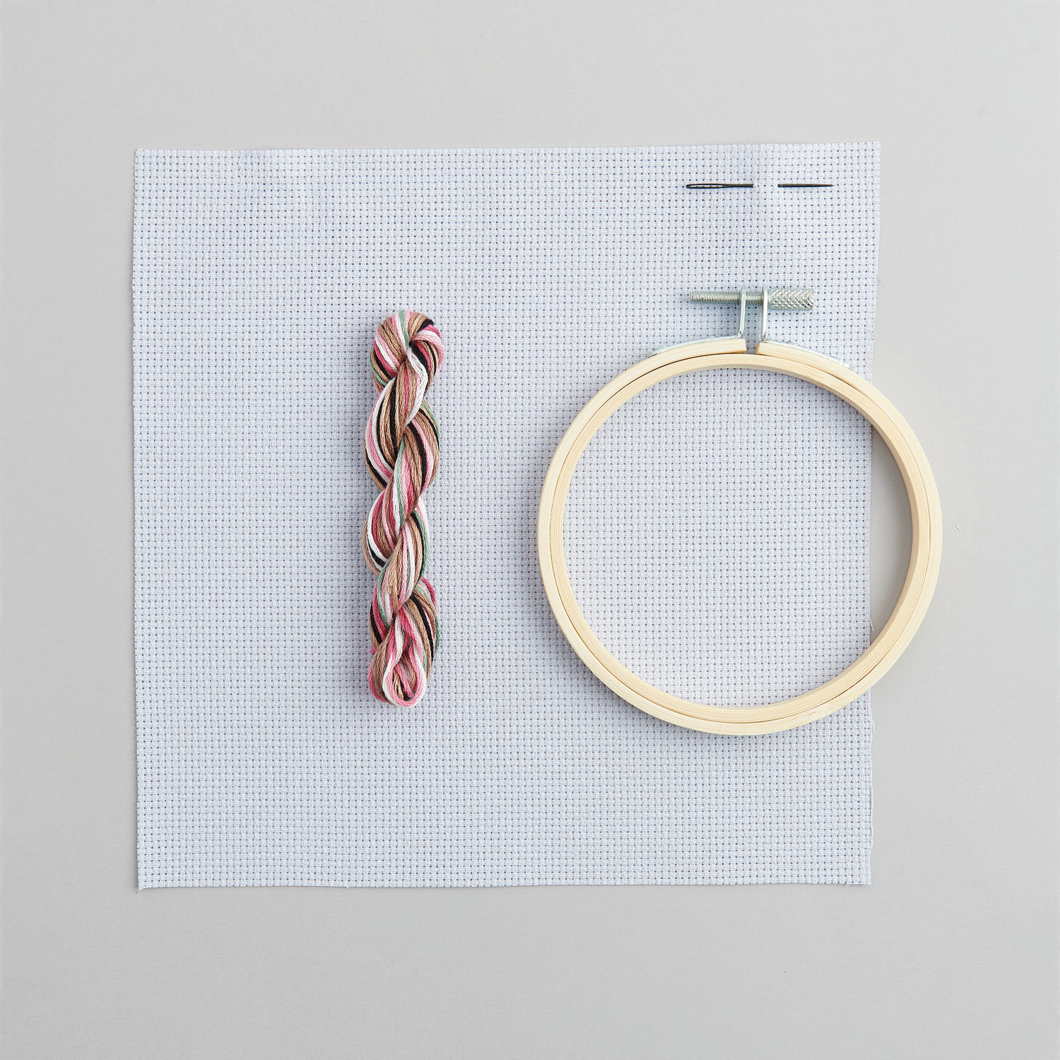 Stickpackung Bild Romantischer Hase: Stickrahmen, Garn und Stoff von Rico Design auf grauem Hintergrund.