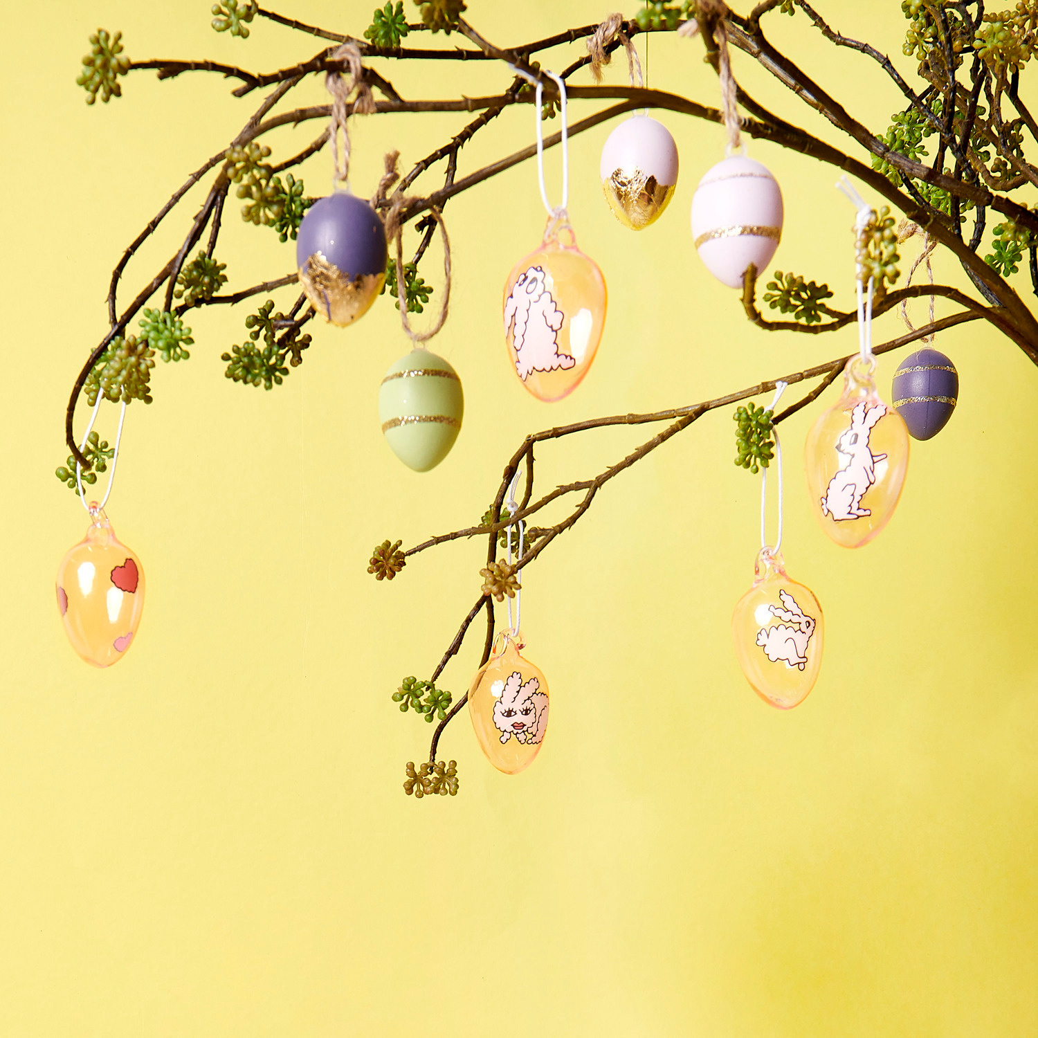 Deko-Eier Set Goldstreifen: An einem Ast hängen dekorative Eier mit Hasenmotiven und Goldstreifen. Ideal für festliche Dekorationen.