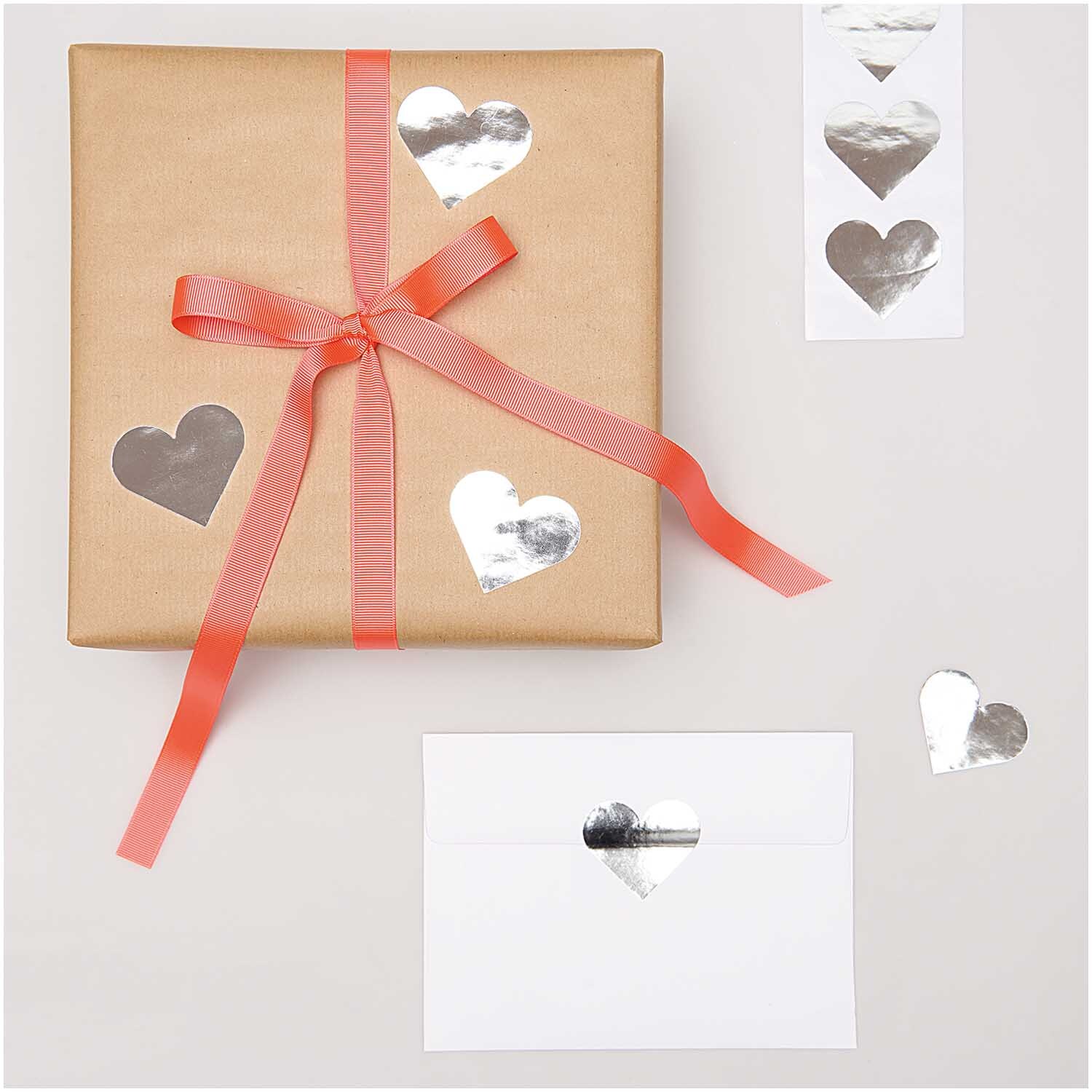 Paper Poetry Sticker Herzen dekorieren ein Geschenk und Umschlag mit glänzenden silbernen Herzmotiven. Ideal für kreative Verpackungen.
