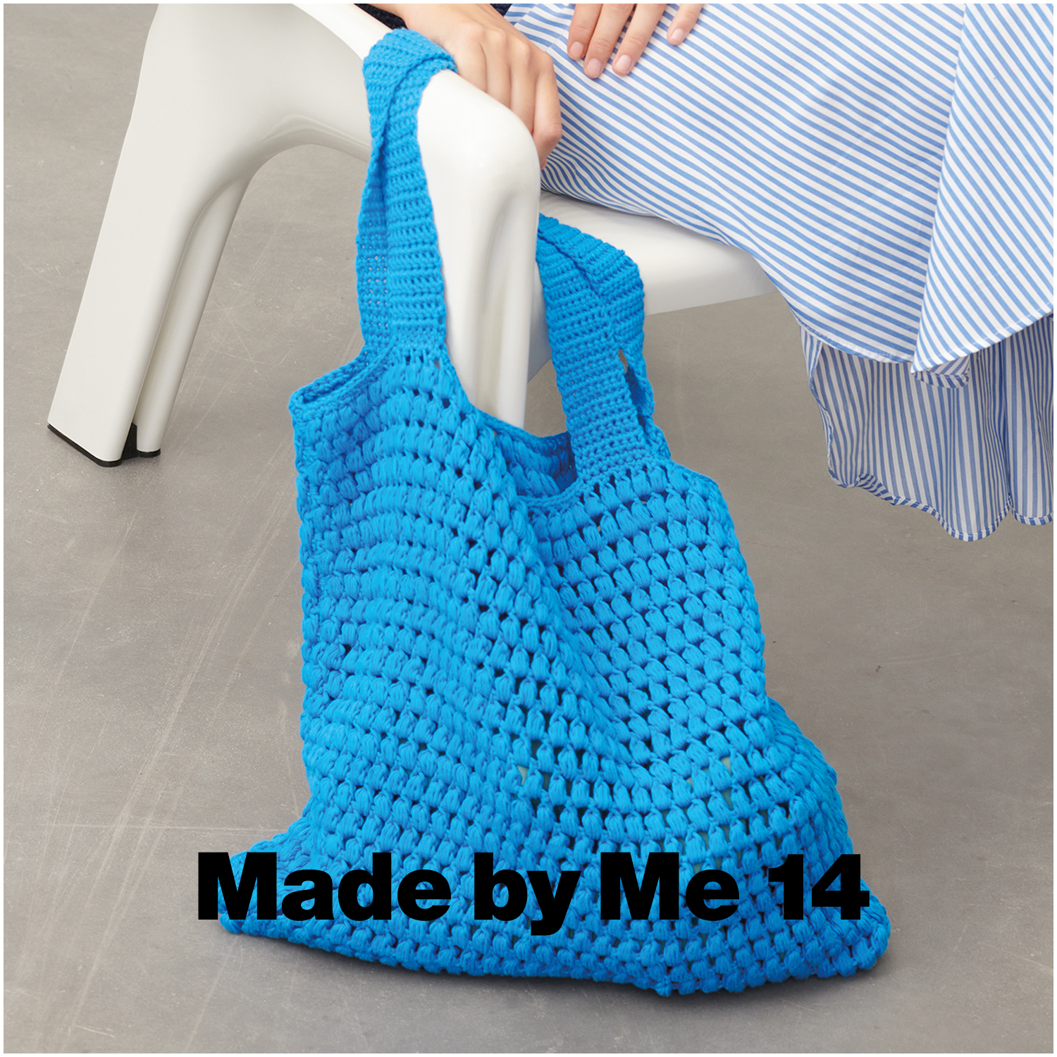 Creative Cotton aran: Gehäkelte blaue Tasche aus Rico Design Garn, platziert auf einem weißen Stuhl.