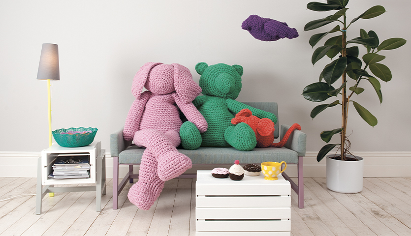 Häkelanleitung XXL Hase aus Creative Loopy: Rosa gehäkelter Hase auf Sofa neben grünem Bär, dekoriert mit Pflanzen und Lampen.