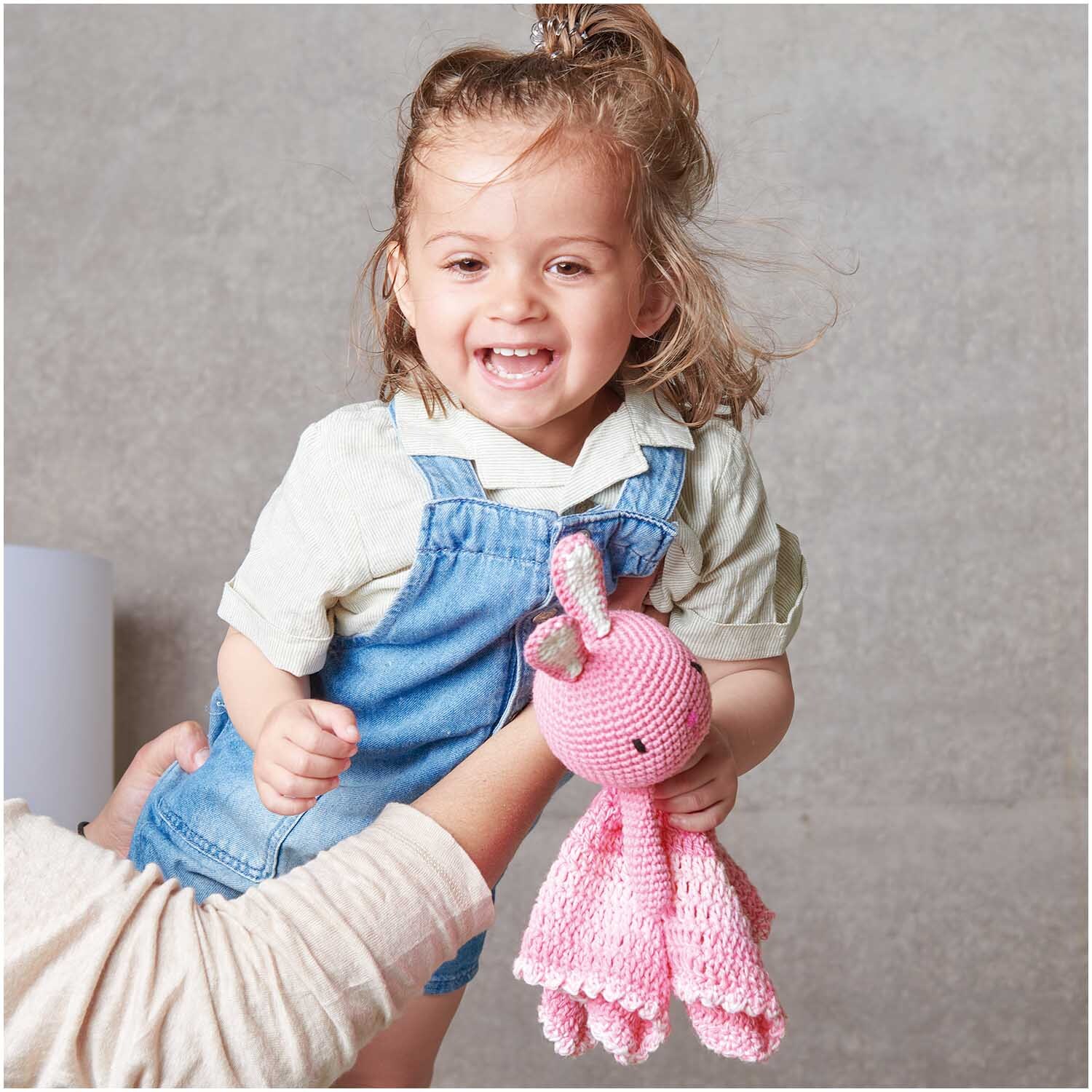 Häkelset Ricorumi Baby Blankies Hase: Ein Kind hält ein rosa gehäkeltes Kuscheltier von Rico Design.