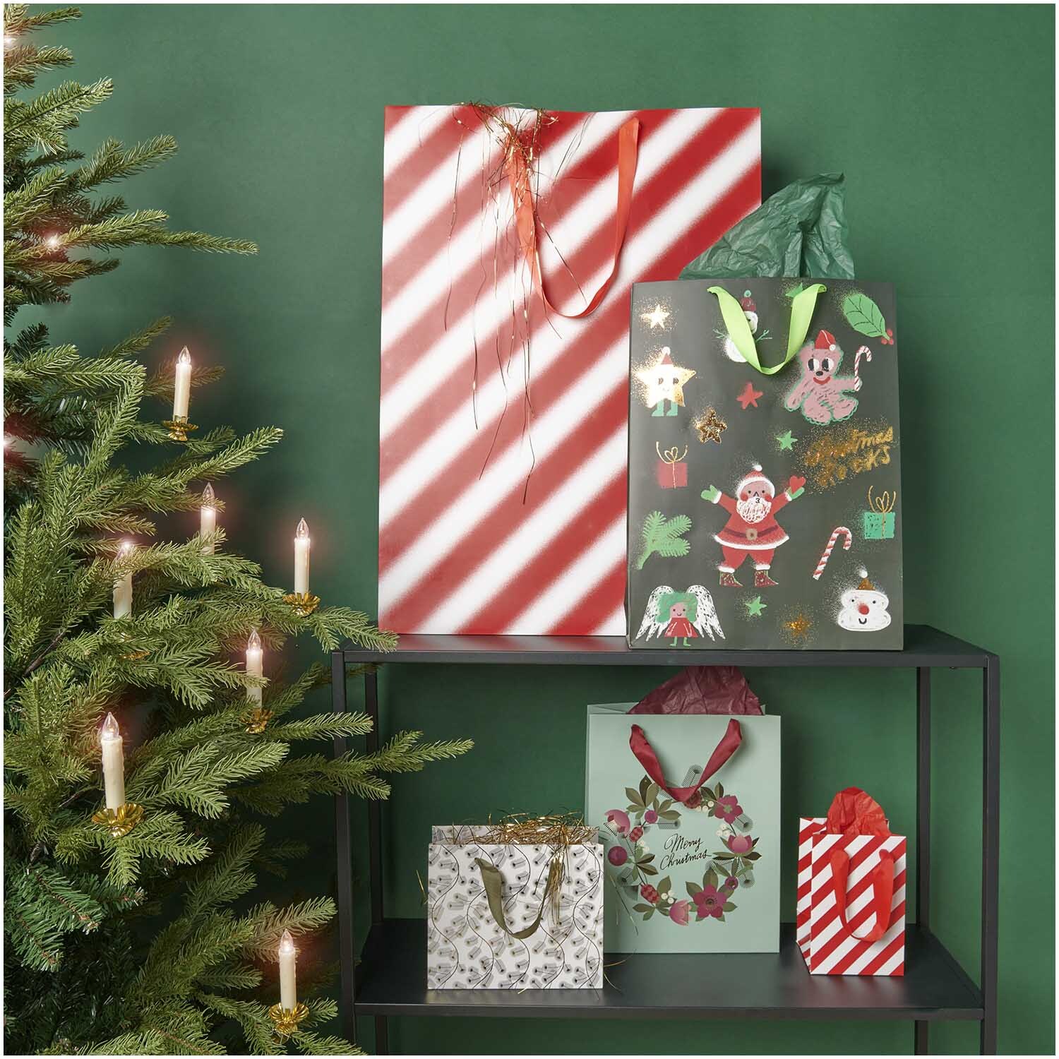 Paper Poetry Geschenktüte in festlichem Design, umgeben von Weihnachtsdekoration auf einem Regal.