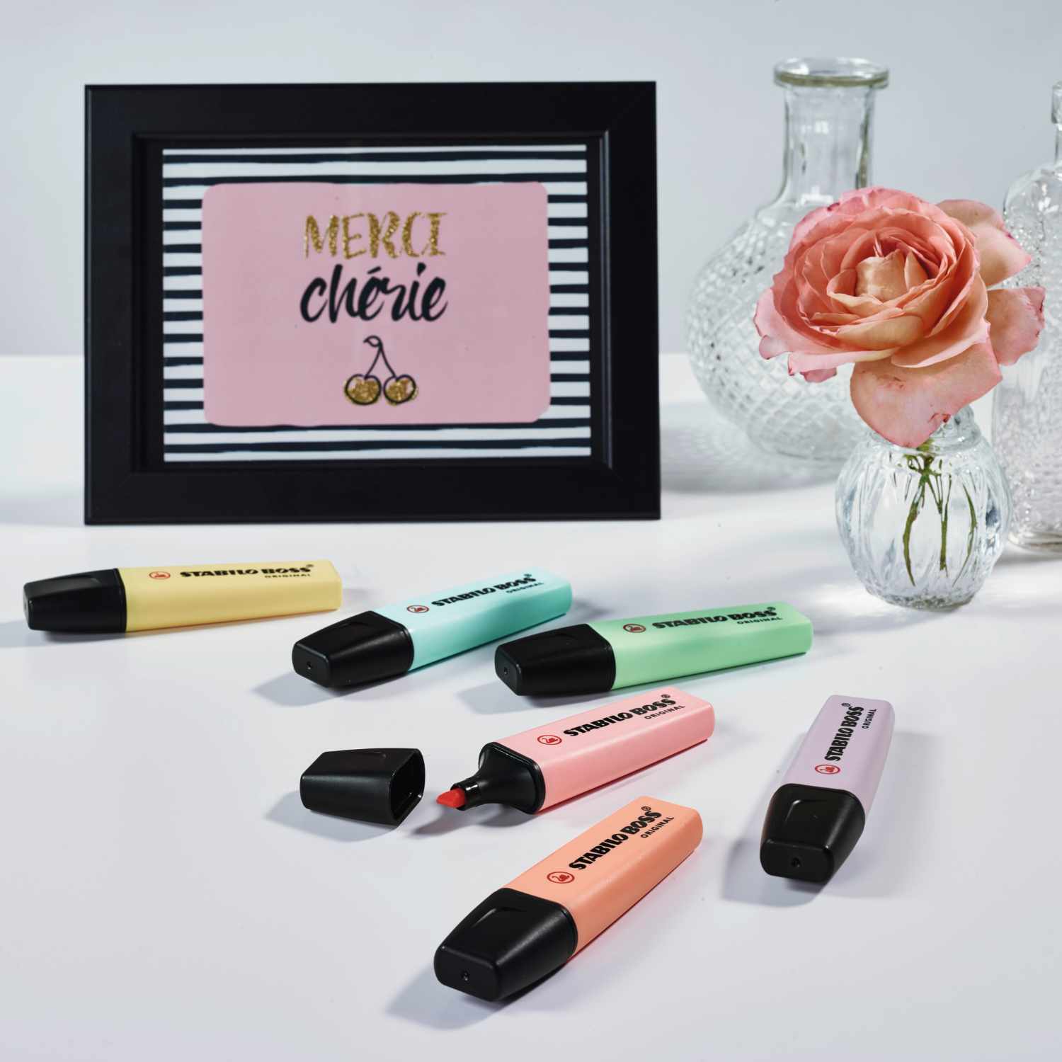 Textmarker Boss Original Pastell 4 Stück von STABILO in verschiedenen Farben neben einem gerahmten Bild und einer Rose.