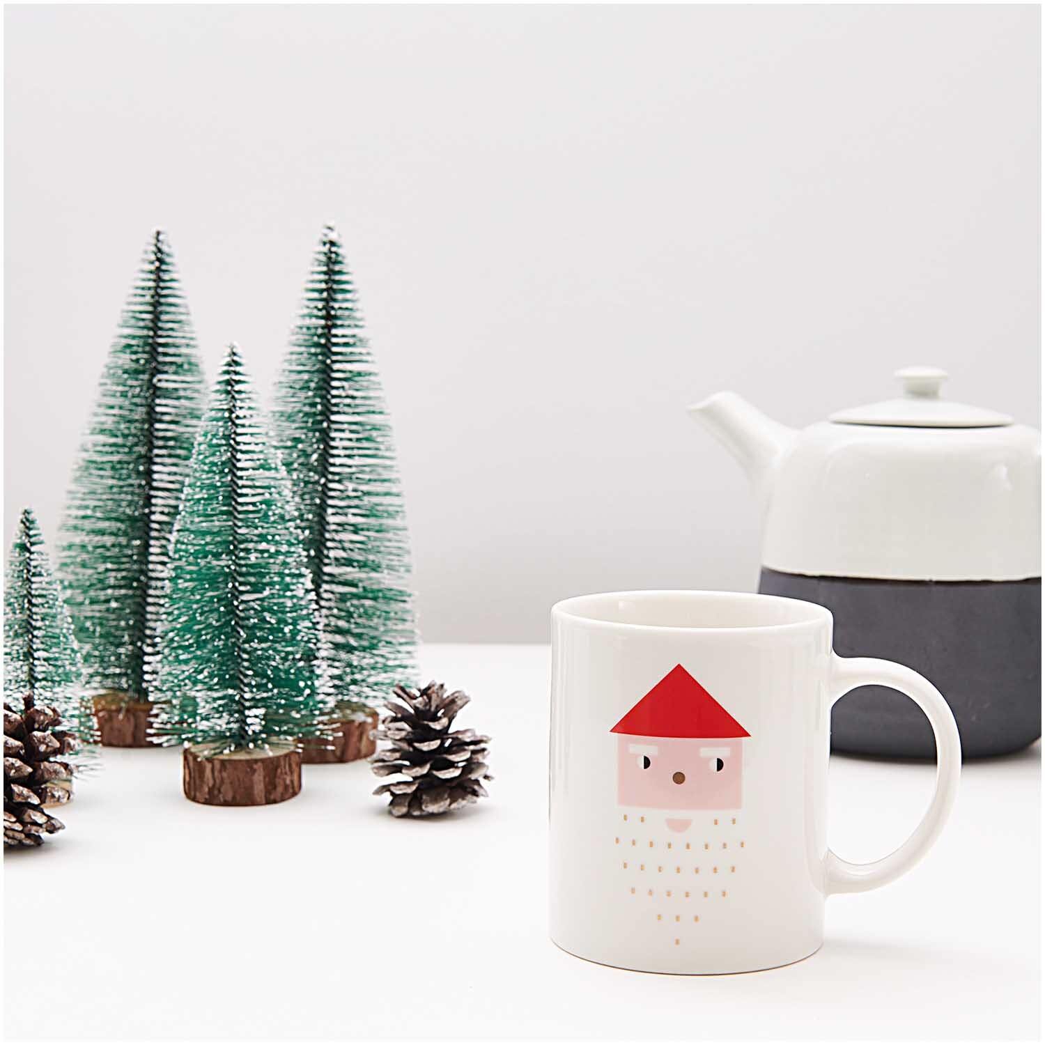 Porzellan Tasse Santa 8x9,5cm mit rotem Santa-Motiv, neben grünen Miniaturtannen und weißer Teekanne.