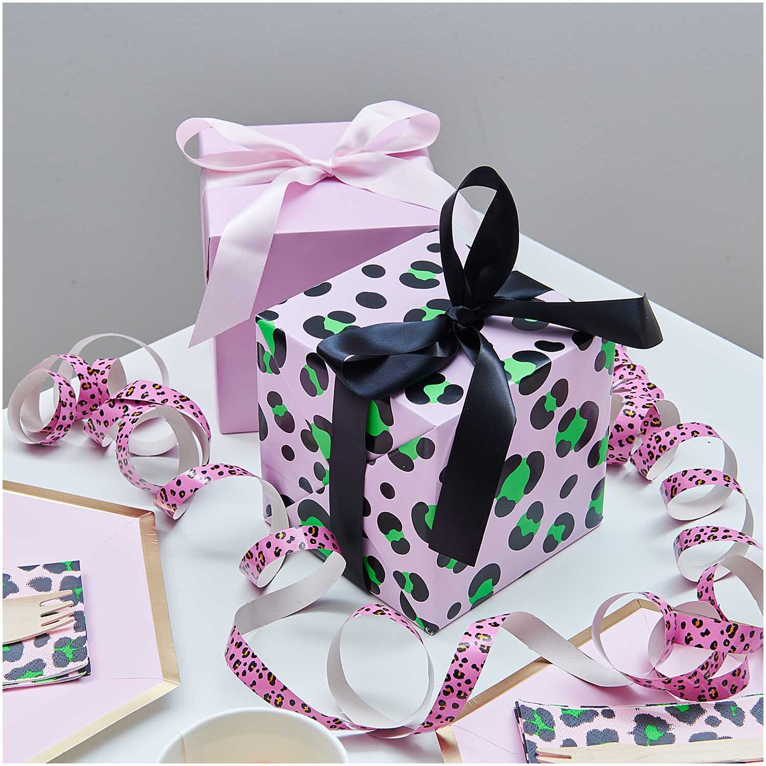 Paper Poetry Geschenkpapier Acid Leo rosa zeigt ein Geschenk mit schwarzer Schleife und rosa Hintergrund. Ideal für stilvolle Verpackungen.