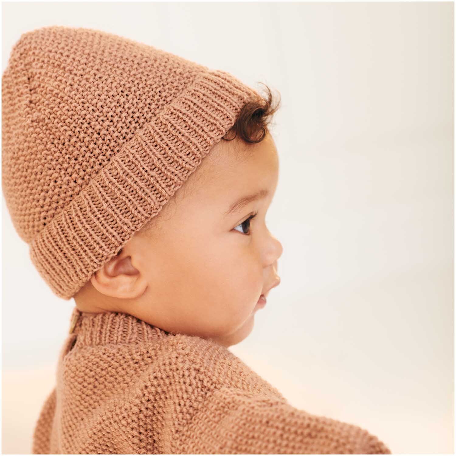 Baby Merino: Ein Baby trägt eine gestrickte Mütze und Pullover in Puderfarbe, aus weicher Wolle.