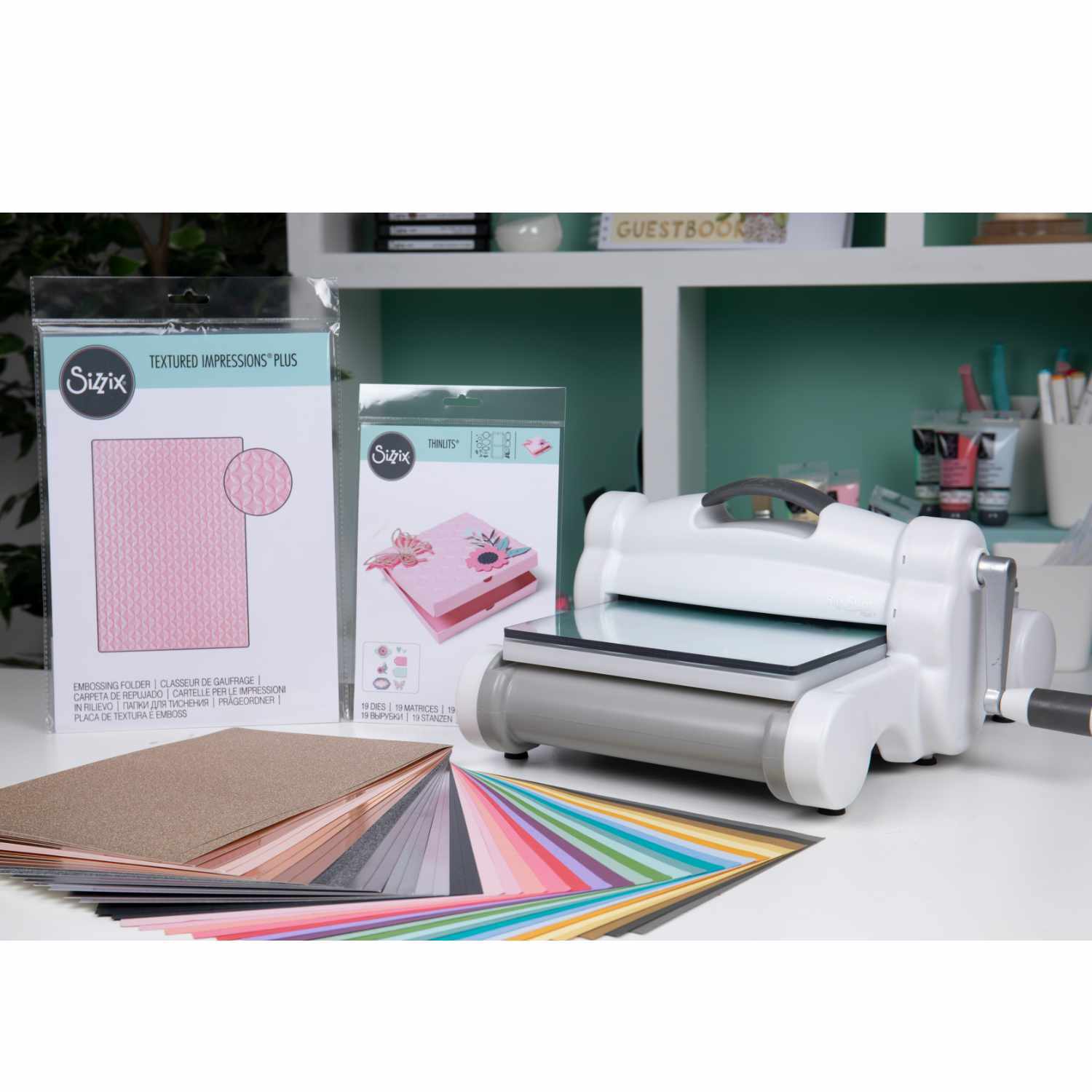 Big Shot Plus Starter Set: Weiße Prägemaschine von Sizzix mit A4-Papier und Zubehör in verschiedenen Farben auf einem Tisch. Ideal für Bastelprojekte.
