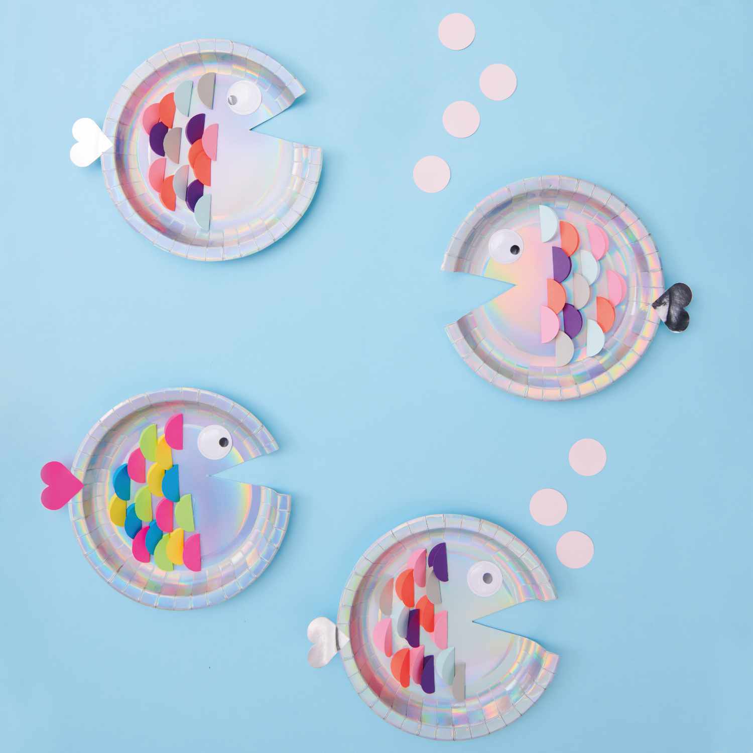 Bastelanleitung Fische aus Papptellern: Vier bunte Pappteller-Fische auf blauem Hintergrund mit bunten Schuppen und Herzen.