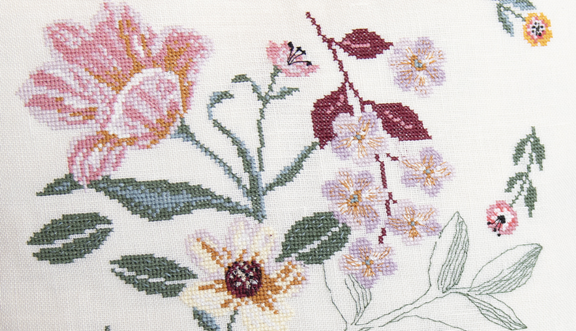 Stickanleitung florales Kissen gestalten: Detailreiche Stickerei mit bunten Blumenmotiven auf hellem Stoff. Ideal für kreative Heimdekoration.