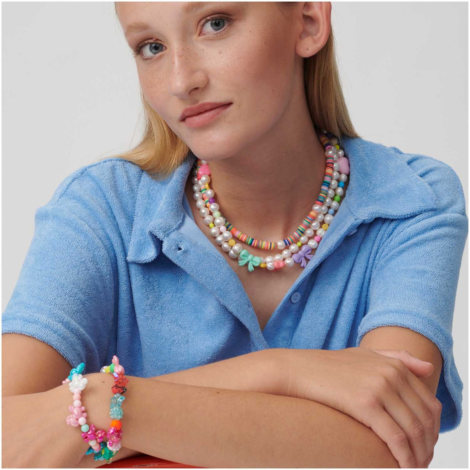 itoshii Perlen Bundle pastell 10mm 20 Stück: Frau trägt bunte Perlenketten und Armbänder von Rico Design, passend zu blauem Oberteil.