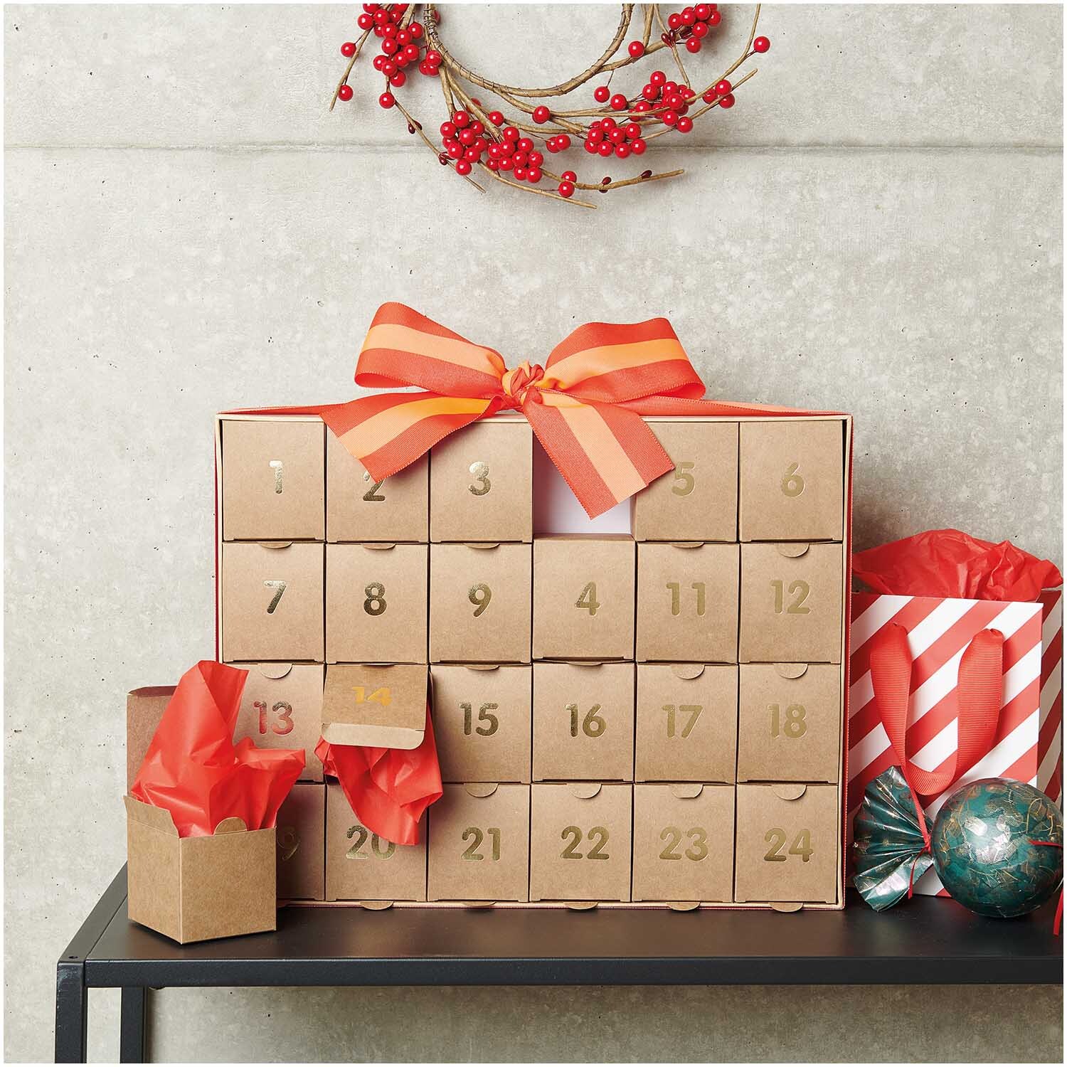 Adventskalender zum Befüllen aus Kraftpapier-Gold mit roten Schleifen, dekoriert auf einem Tisch.