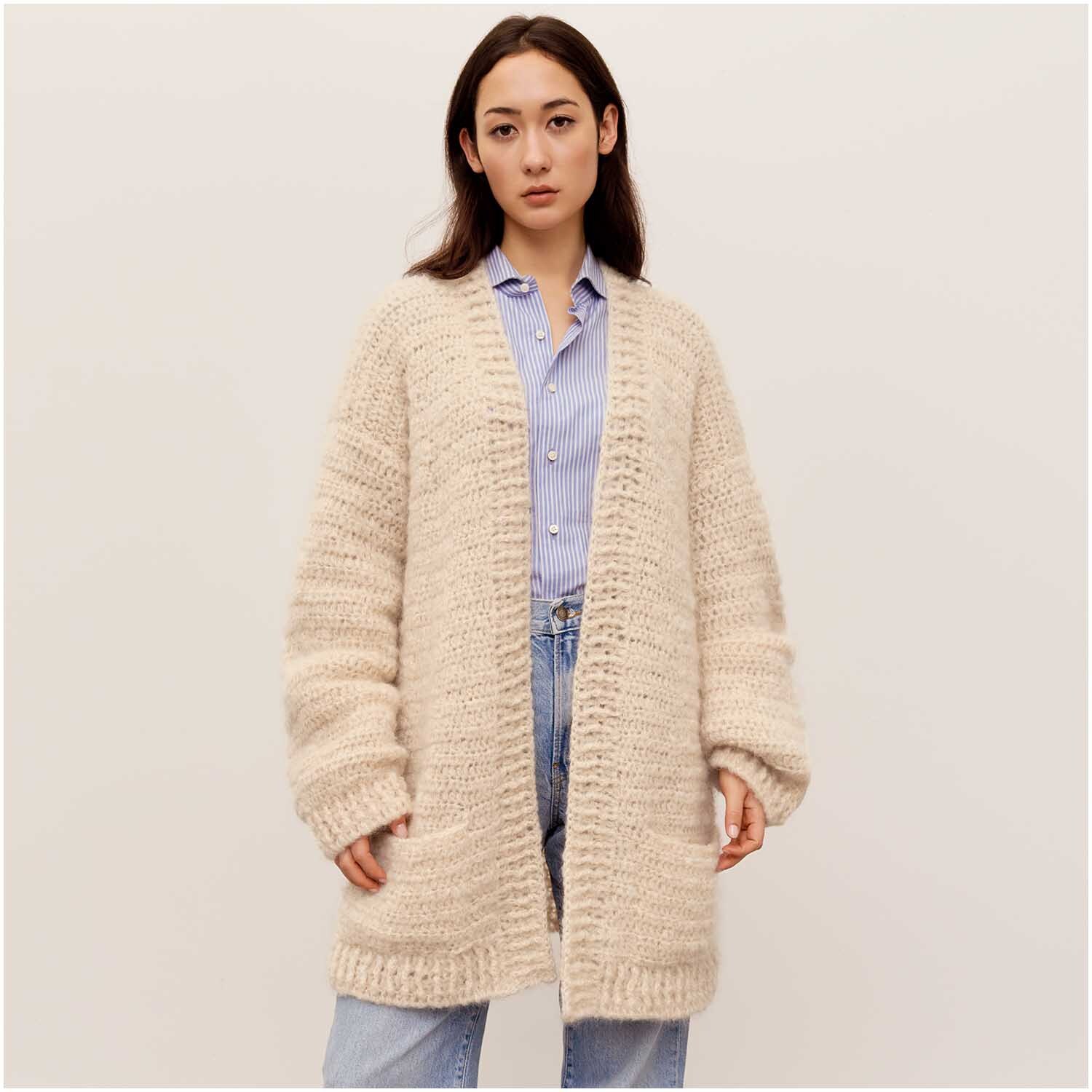 Häkelset Cardigan Modell 03: Frau trägt beigen, grob gestrickten Cardigan über blauer Bluse und Jeans.