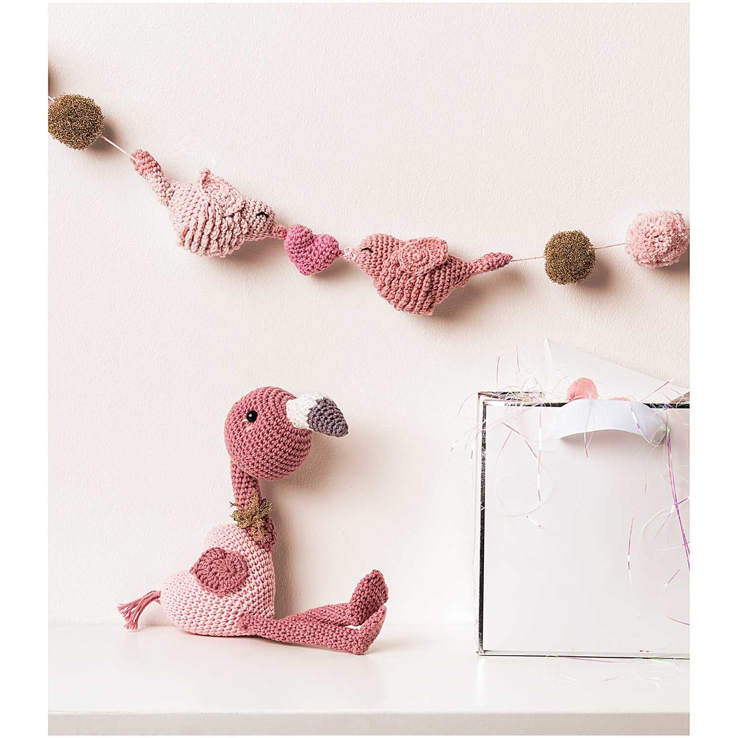 Creative Ricorumi dk: Ein altrosa gehäkelter Flamingo von Rico Design sitzt vor einer Girlande aus Tieren und Pompons.