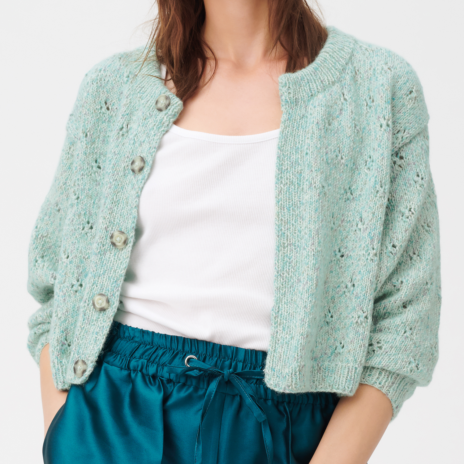 Strickanleitung Jacke aus Creative Cotton Flecky Fleece: Mintgrüne Strickjacke mit Knöpfen, kombiniert mit weißem Top und blauer Hose.